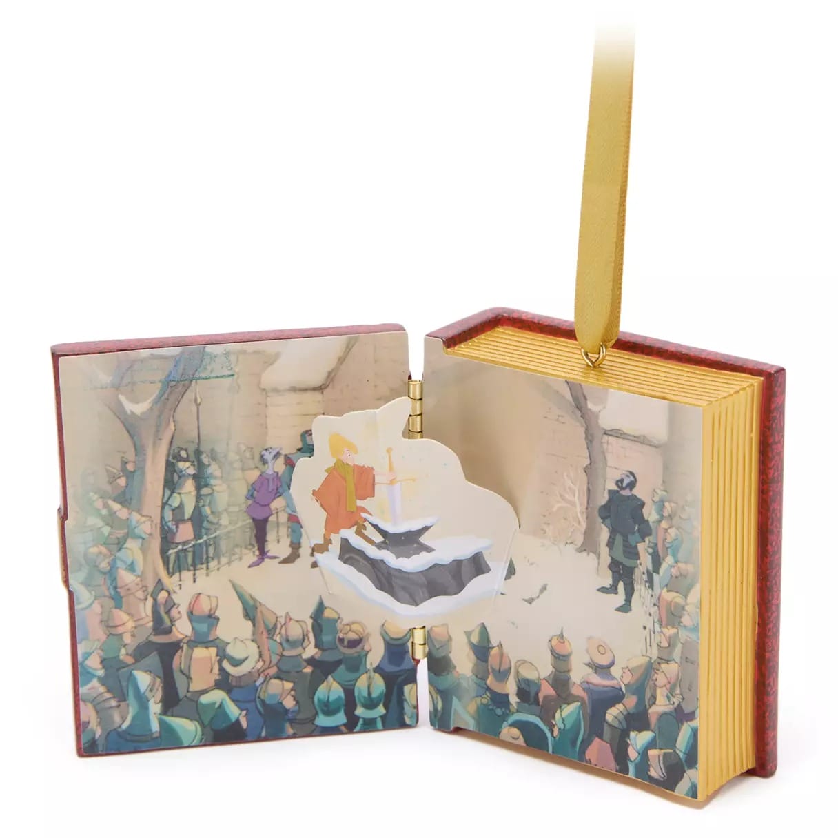 An open storybook ornament with a pop-up sword-in-the-stone scene and gold-edged pages, hanging from a gold ribbon.