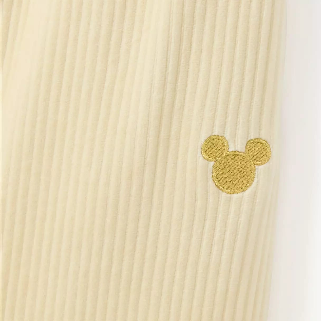 Beige ribbed fabric with a small yellow outline of a mouse head embroidered on it.