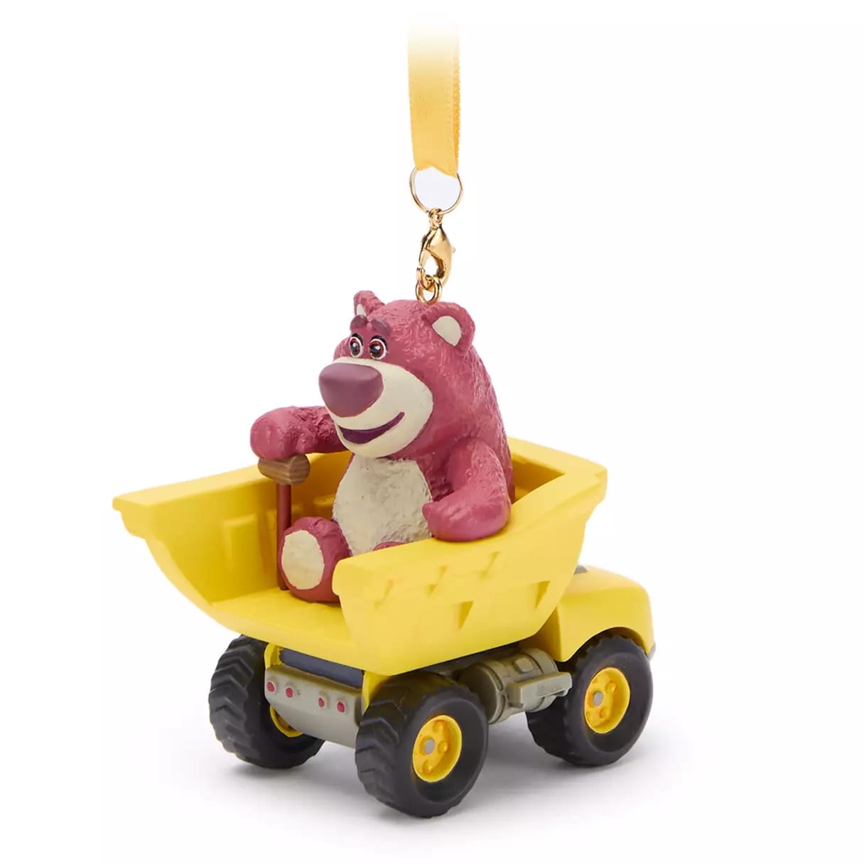 Pink bear figurine sitting in a yellow toy dump truck, attached to a gold ribbon for hanging as an ornament.