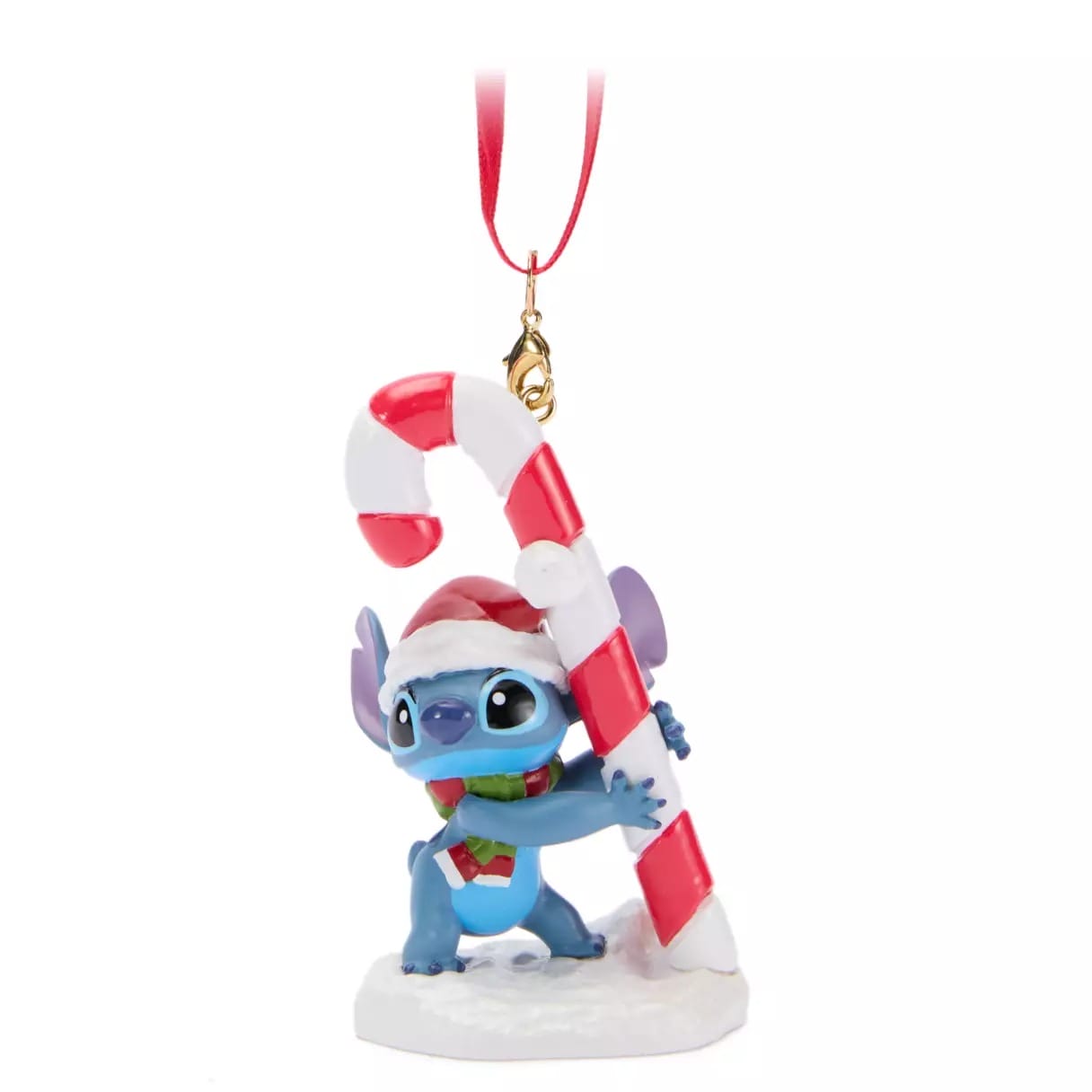 Blue cartoon character Stitch in a Santa hat hugs a large candy cane Christmas ornament with a red ribbon hanger.