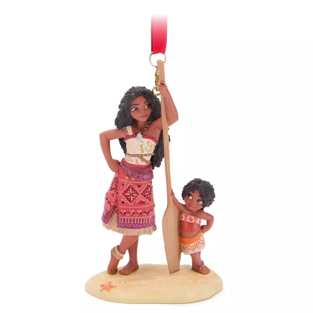 Disney Store ornament of Moana and a young boy on sand, paddle in hand, with a red ribbon—perfect 2025 Christmas merchandise.