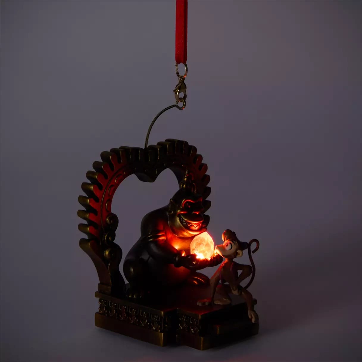 Ornament of a monkey and villain with glowing orb, framed by an arch on a red ribbon—2025 Christmas merchandise at Disney Store.