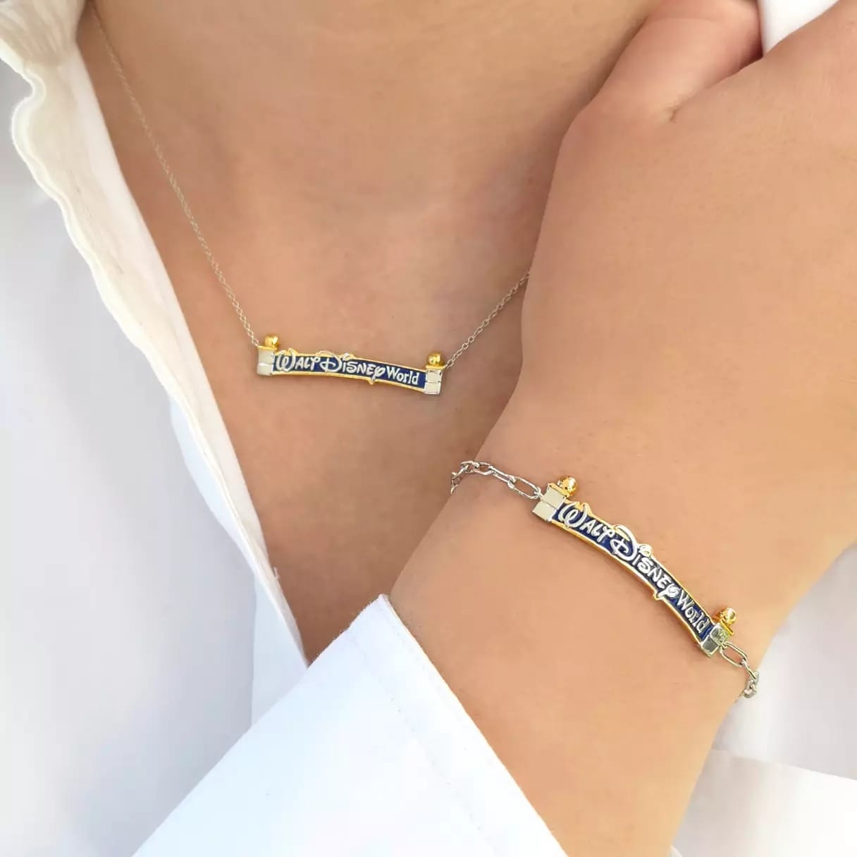 A person in a white shirt showcases a Walt Disney World necklace and bracelet with silver and gold, icons reminiscent of park castles.