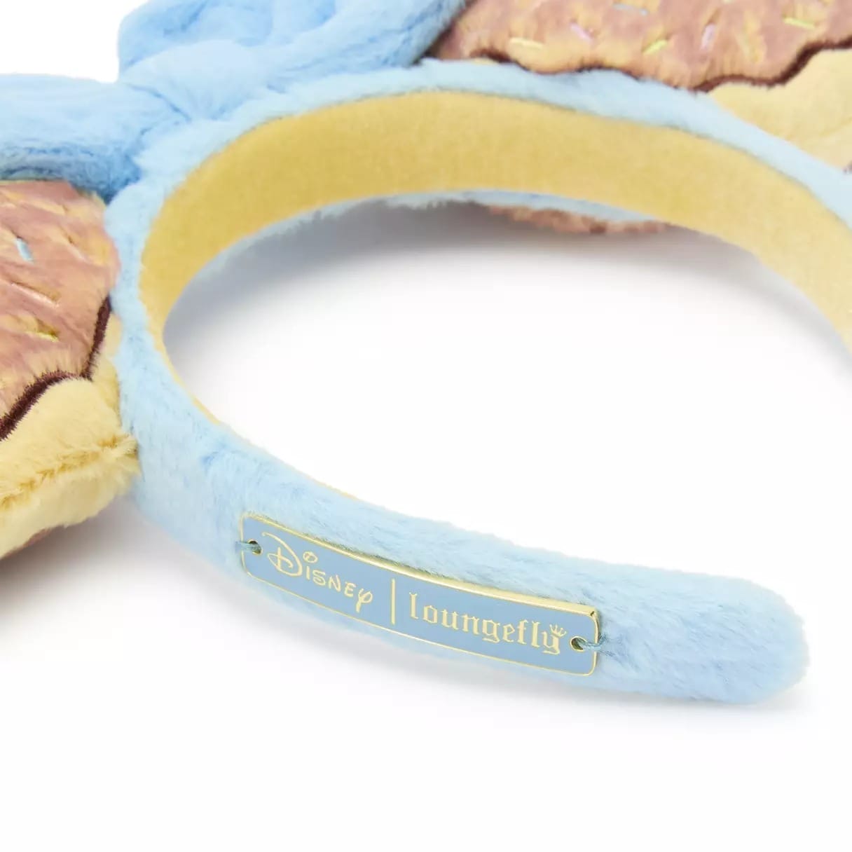 Close-up of a blue Disney Loungefly headband with a gold side label, seen at a Disney park—no castle in the background.
