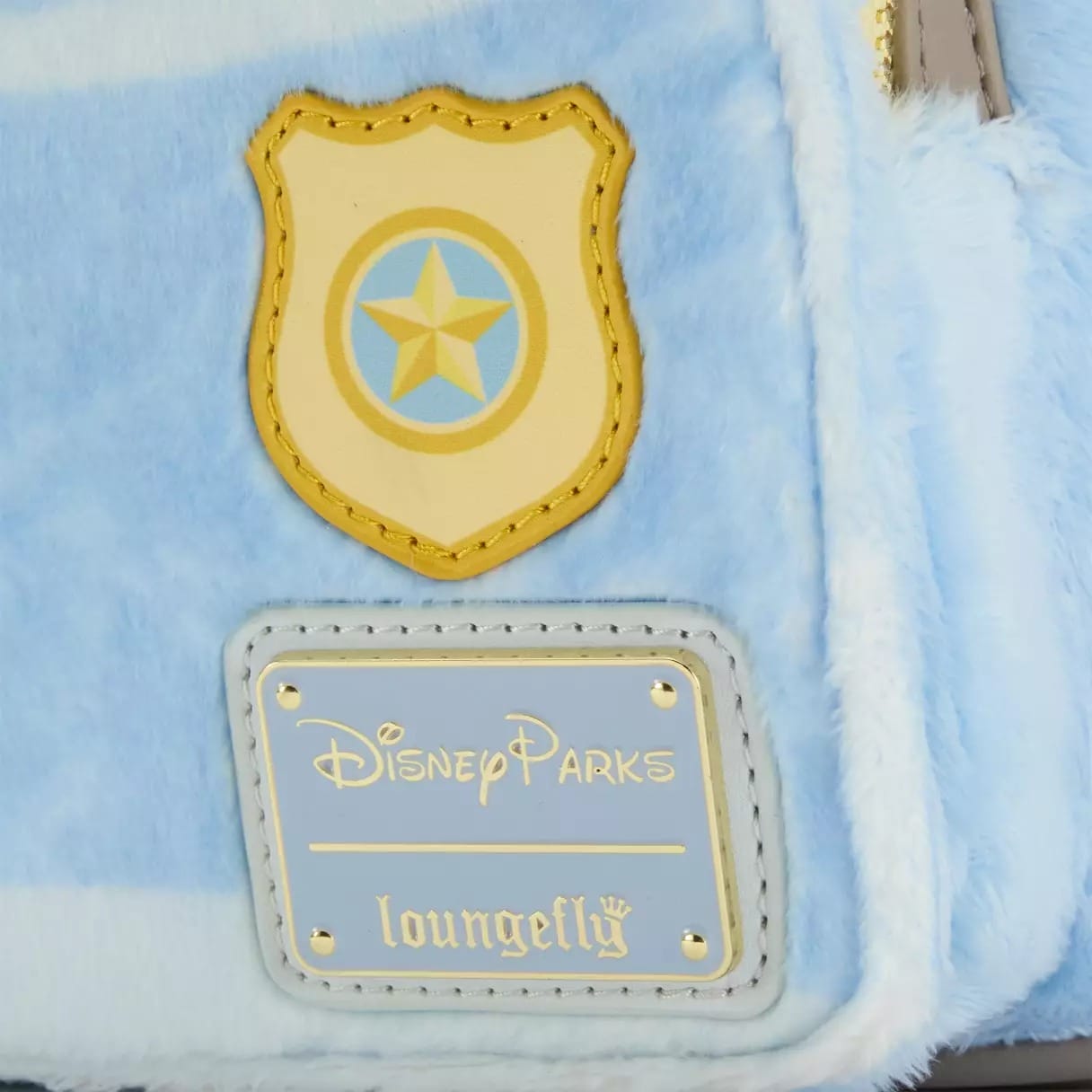Close-up of a light blue fuzzy Disney Parks Loungefly bag, featuring a star badge and gold logo plate—no castle visible here.
