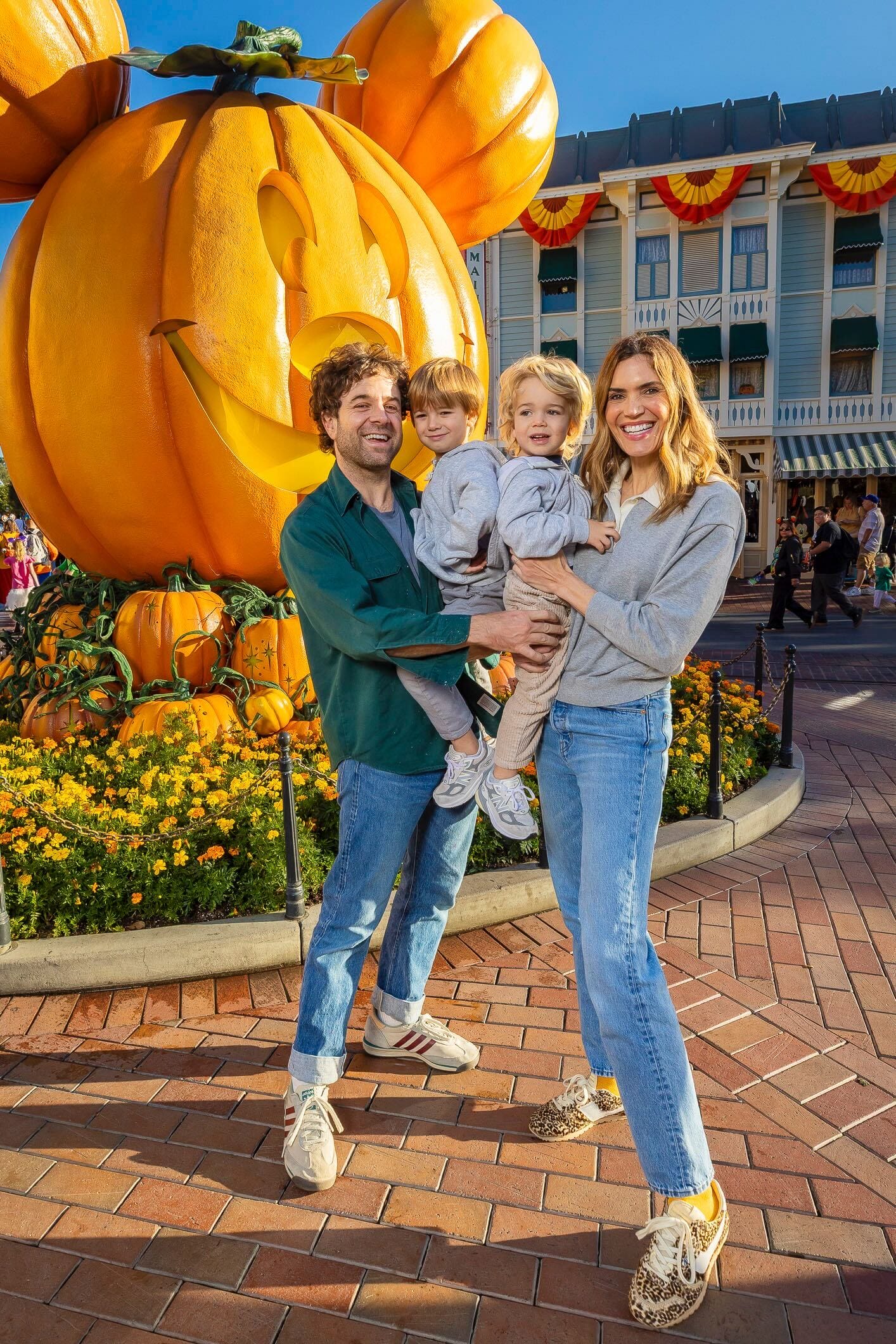 A family of four smiles together in front of a giant Mickey Mouse pumpkin at a Disney park during a festive Halloween celebration.