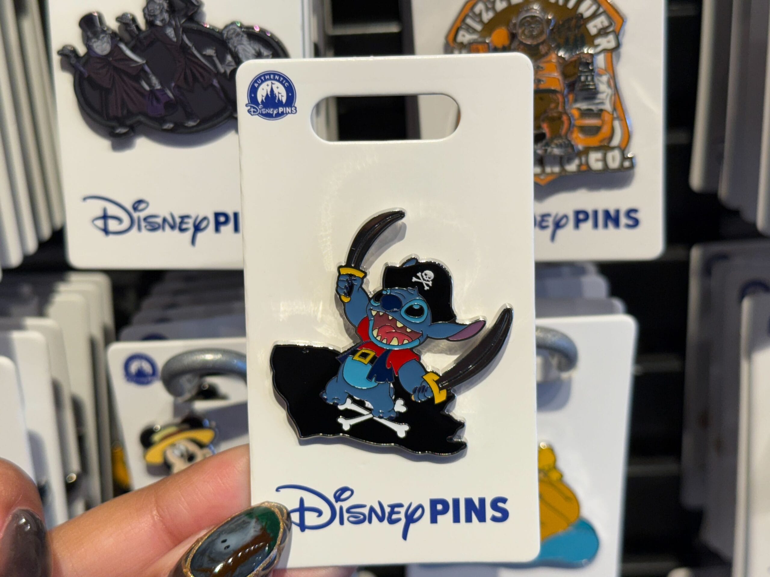 A Disney parks pin shows Stitch in pirate attire, holding two swords, on a Disney Pins card—no castle like those from Disney parks.