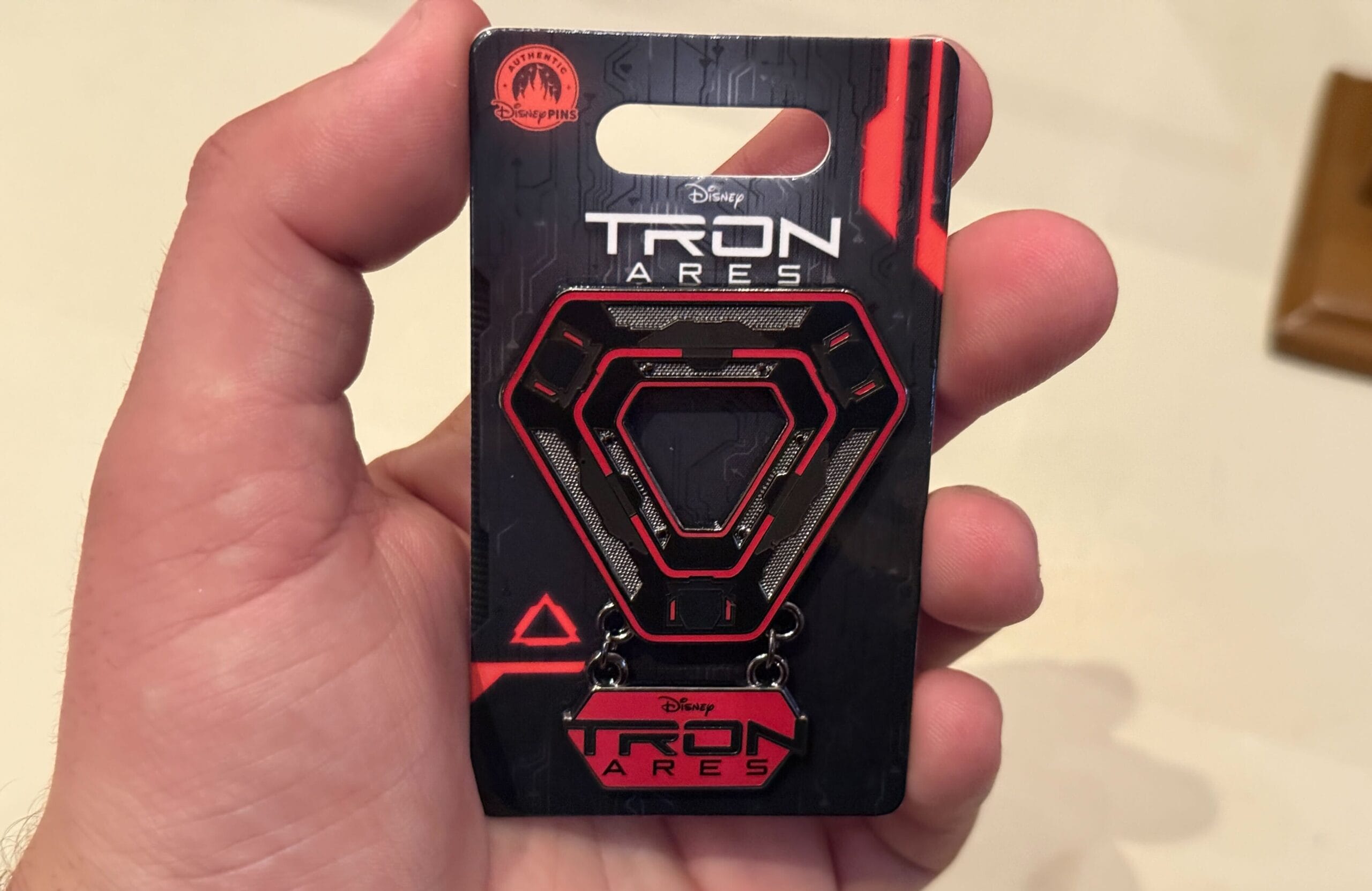 A hand displays a TRON Ares Disney pin on a futuristic red and black backing card, reminiscent of Tomorrowland in Disney Parks.