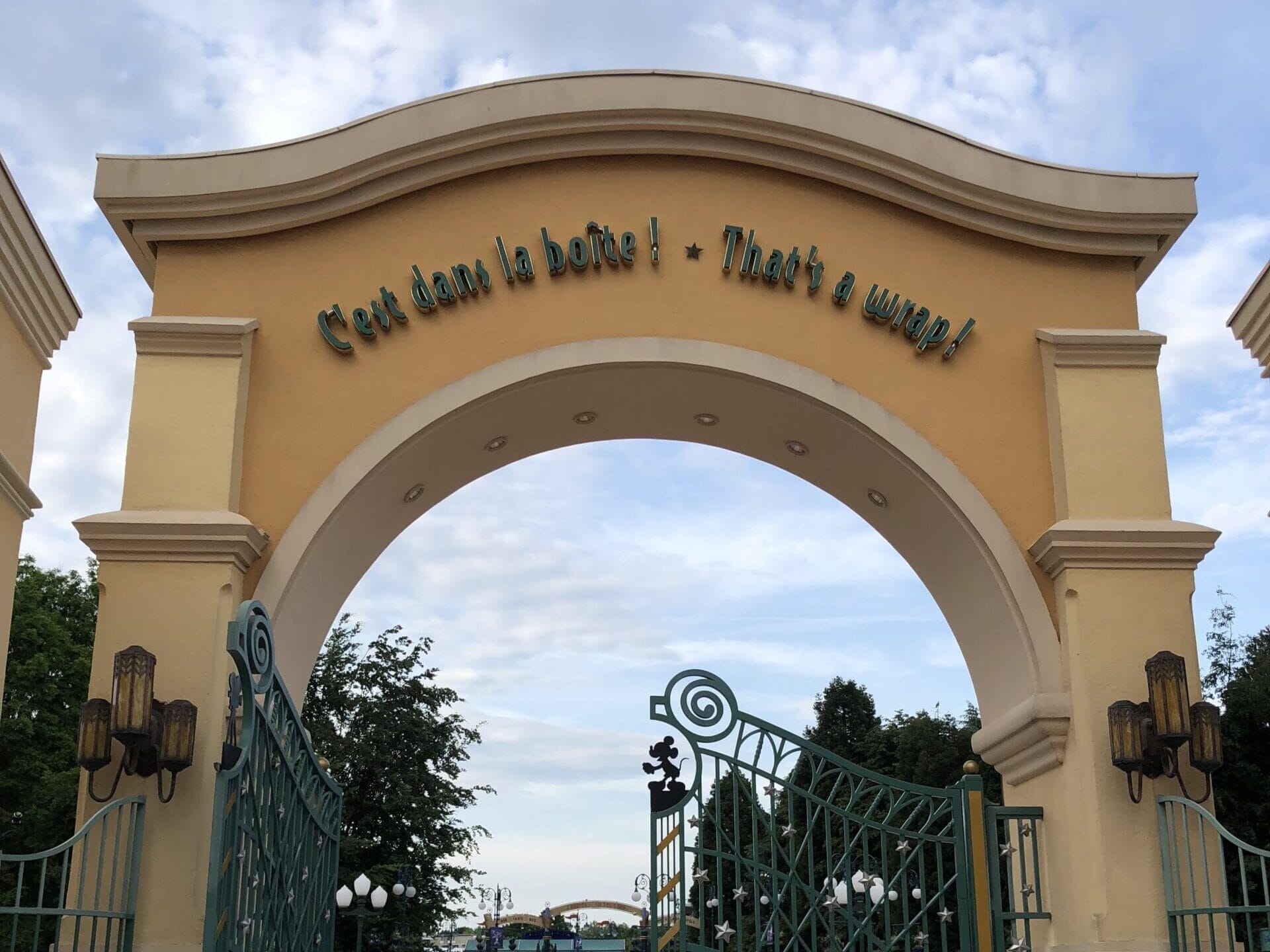 Large yellow archway at Walt Disney Studios, green gates and staff, on a cloudy Disneyland Paris day—no castle in this entrance view.