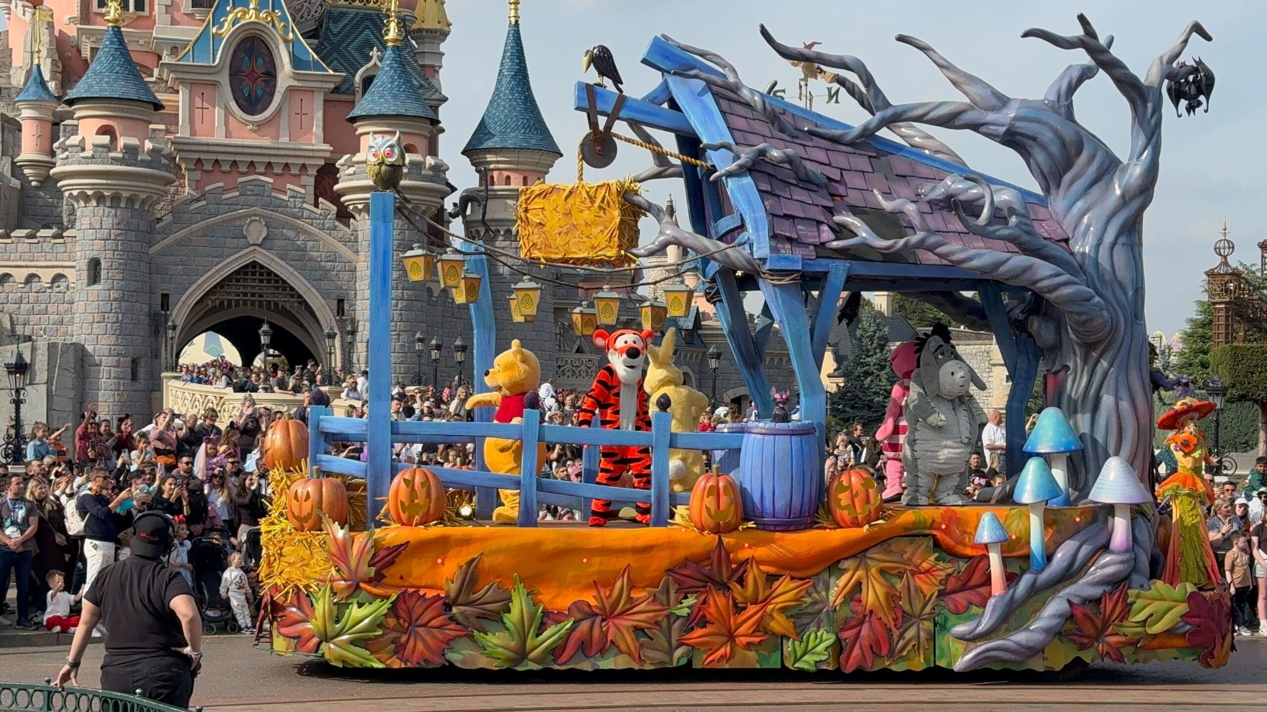 A colorful Parade 2025 float with Winnie the Pooh passes Disneyland Paris castle, part of Mickey’s Halloween Celebration.