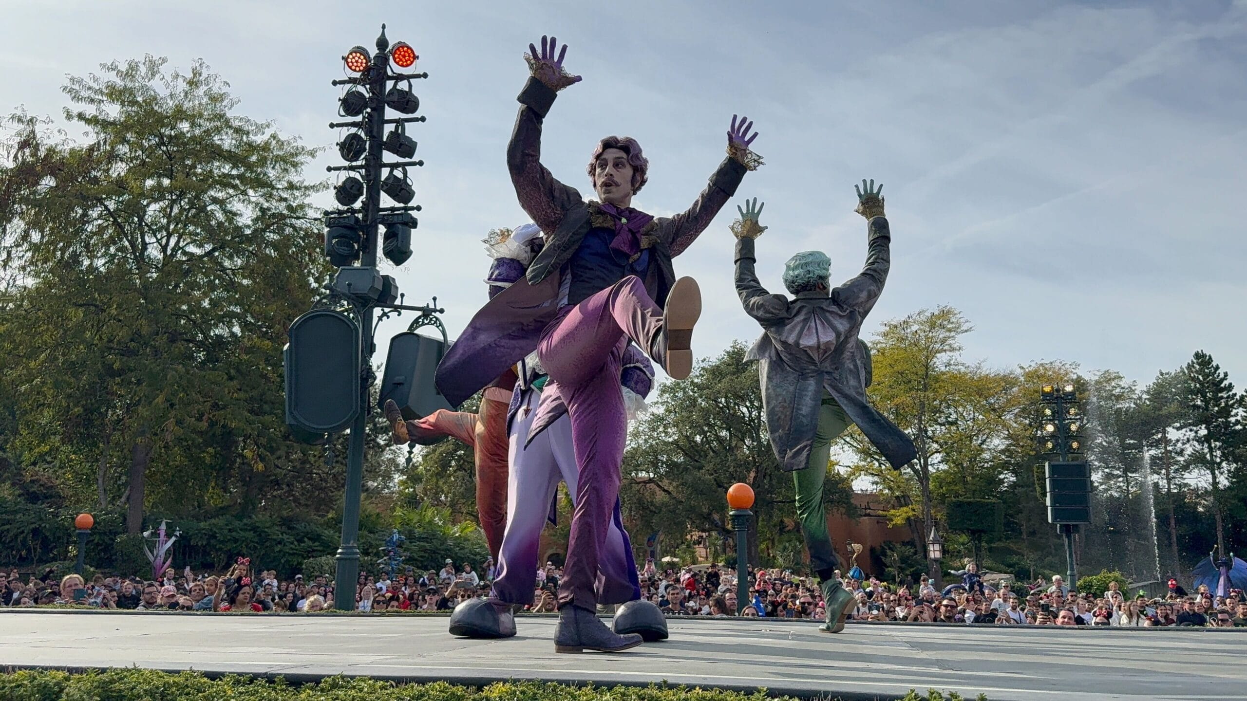 Three performers in colorful costumes dance on stage during Disneyland Paris’s 2025 Mickey’s Halloween Celebration Parade.