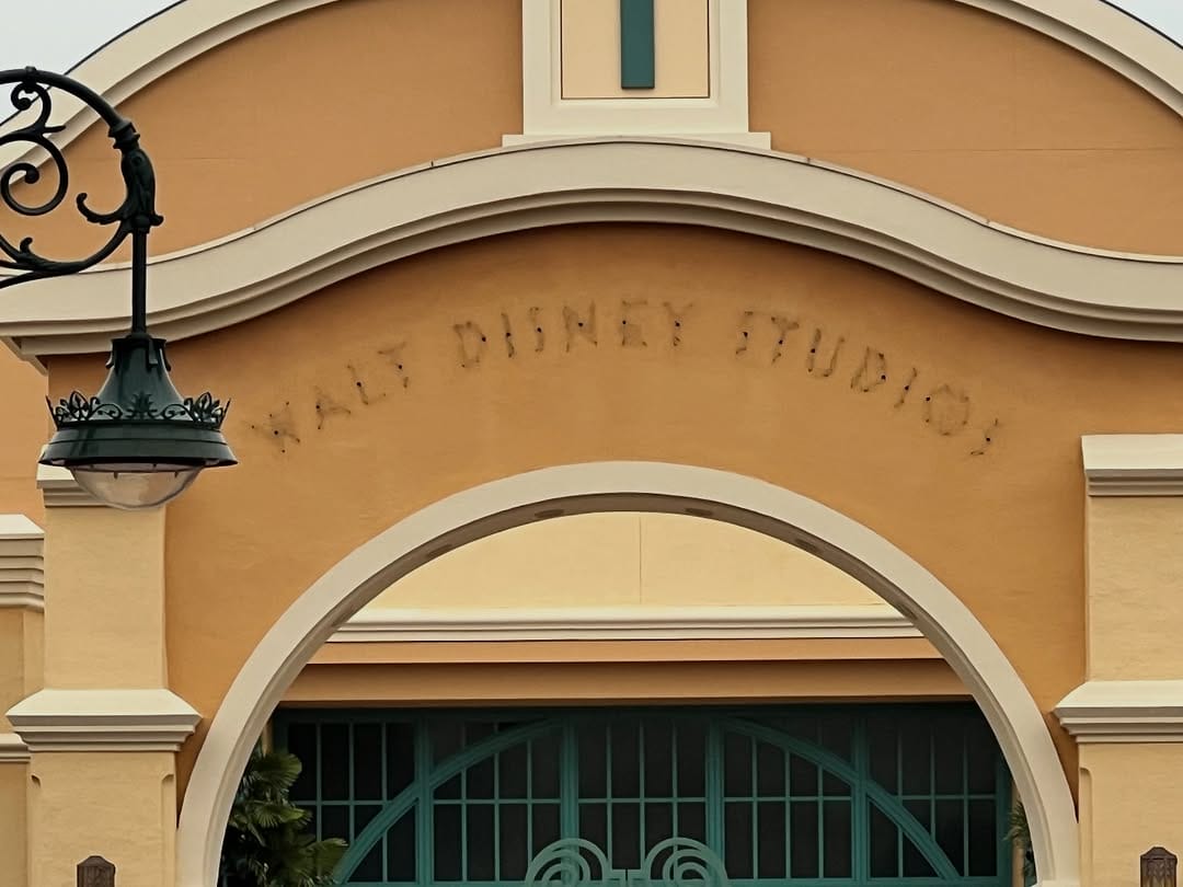 An arched entrance with worn "WALT DISNEY STUDIOS" letters, suggesting a park name change at Disneyland Paris—no castle in view.