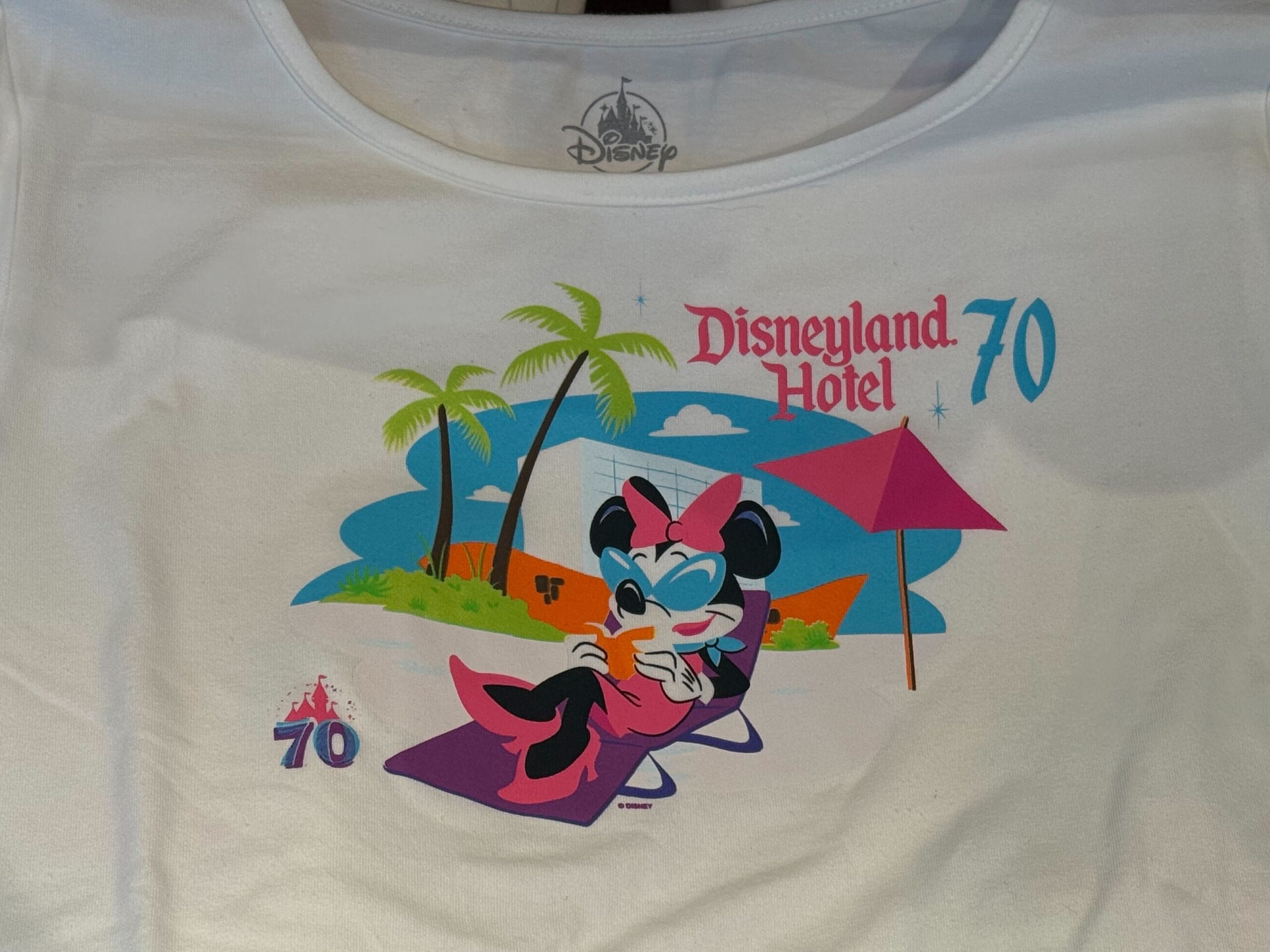 White shirt with Minnie Mouse lounging poolside, "Disneyland Hotel 70th Anniversary" and palm trees in the background.
