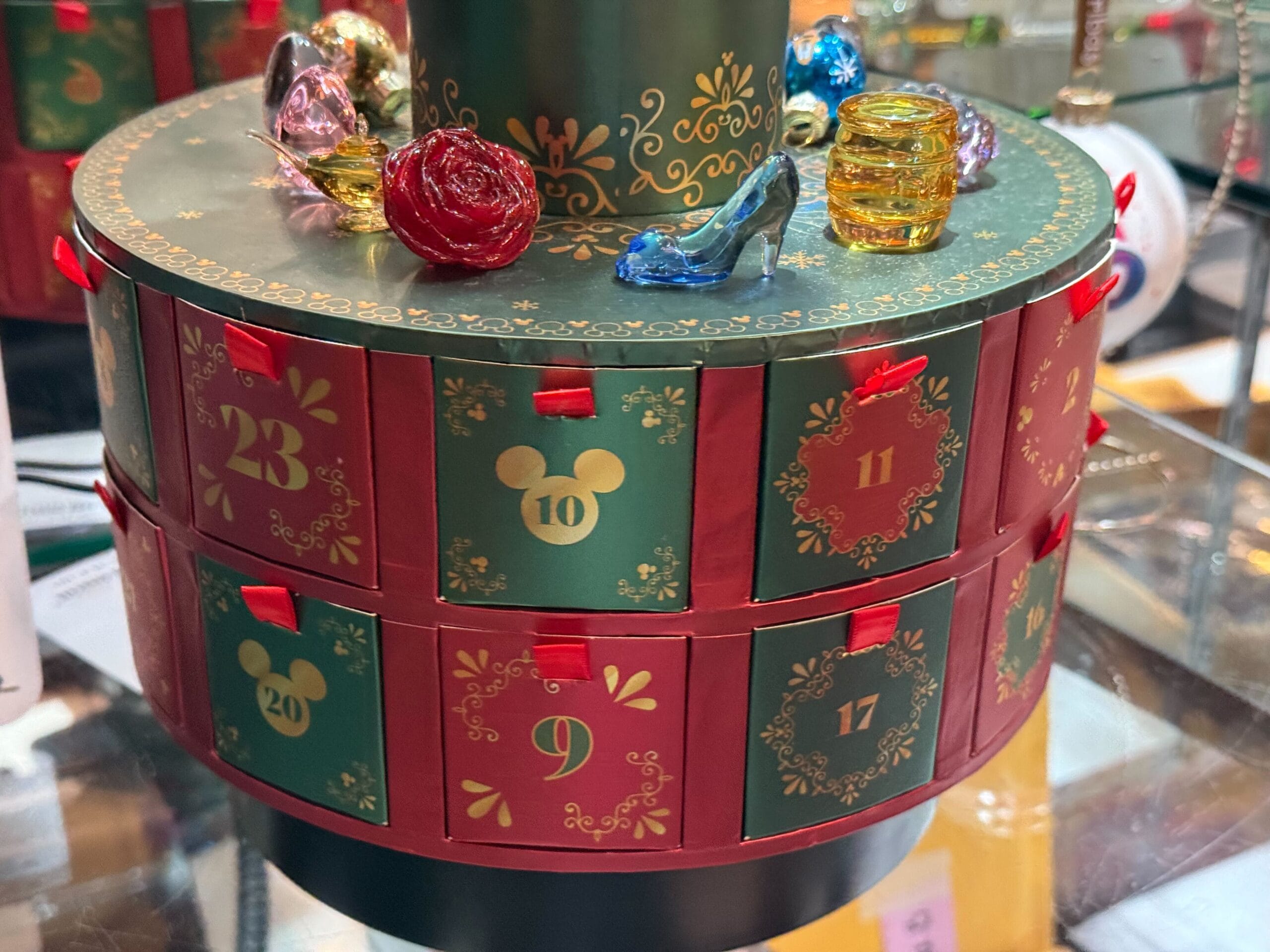 A Disney-themed advent calendar with numbered drawers, topped with glass ornaments like a slipper and rose reminiscent of park icons.