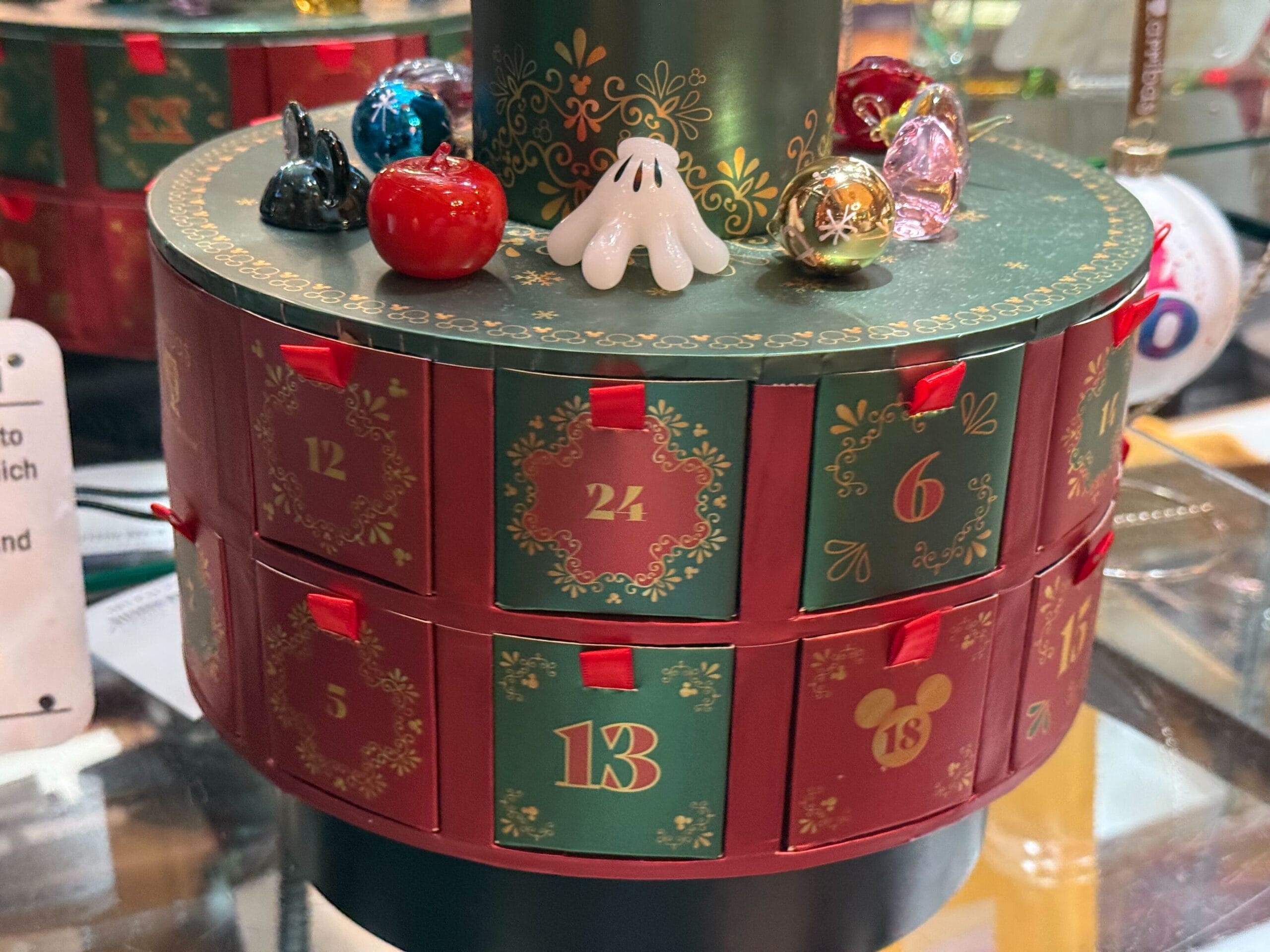A round advent calendar with small numbered drawers, topped by colorful glass figurines, reminiscent of Disney park merchandise displays.