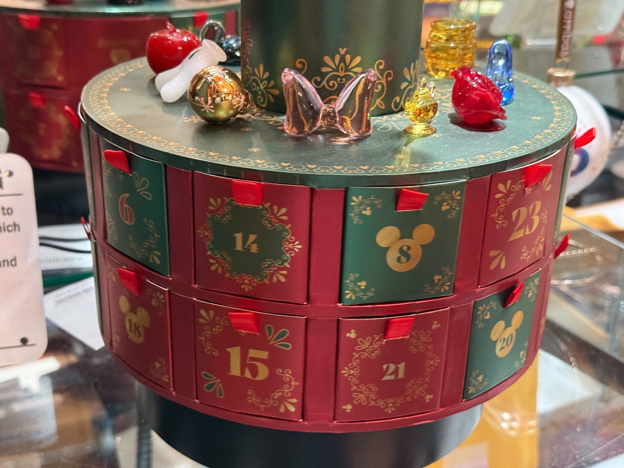 A round Disney parks advent calendar with green and red numbered drawers, topped with small figures like those at Disney castle entrances.