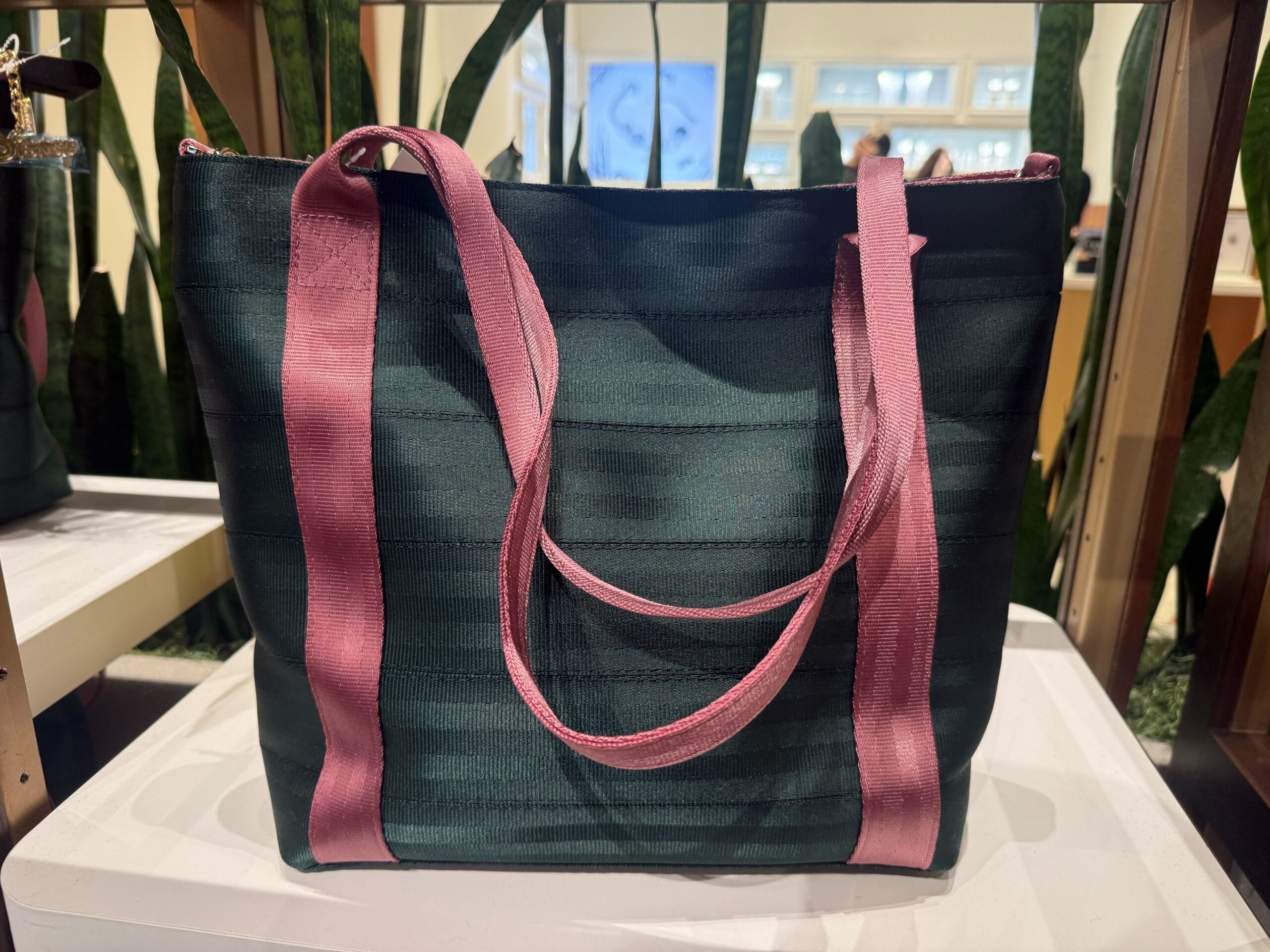 A dark green tote bag with wide pink handles on a white display, reminiscent of Disney Parks’ colorful merchandise shops.