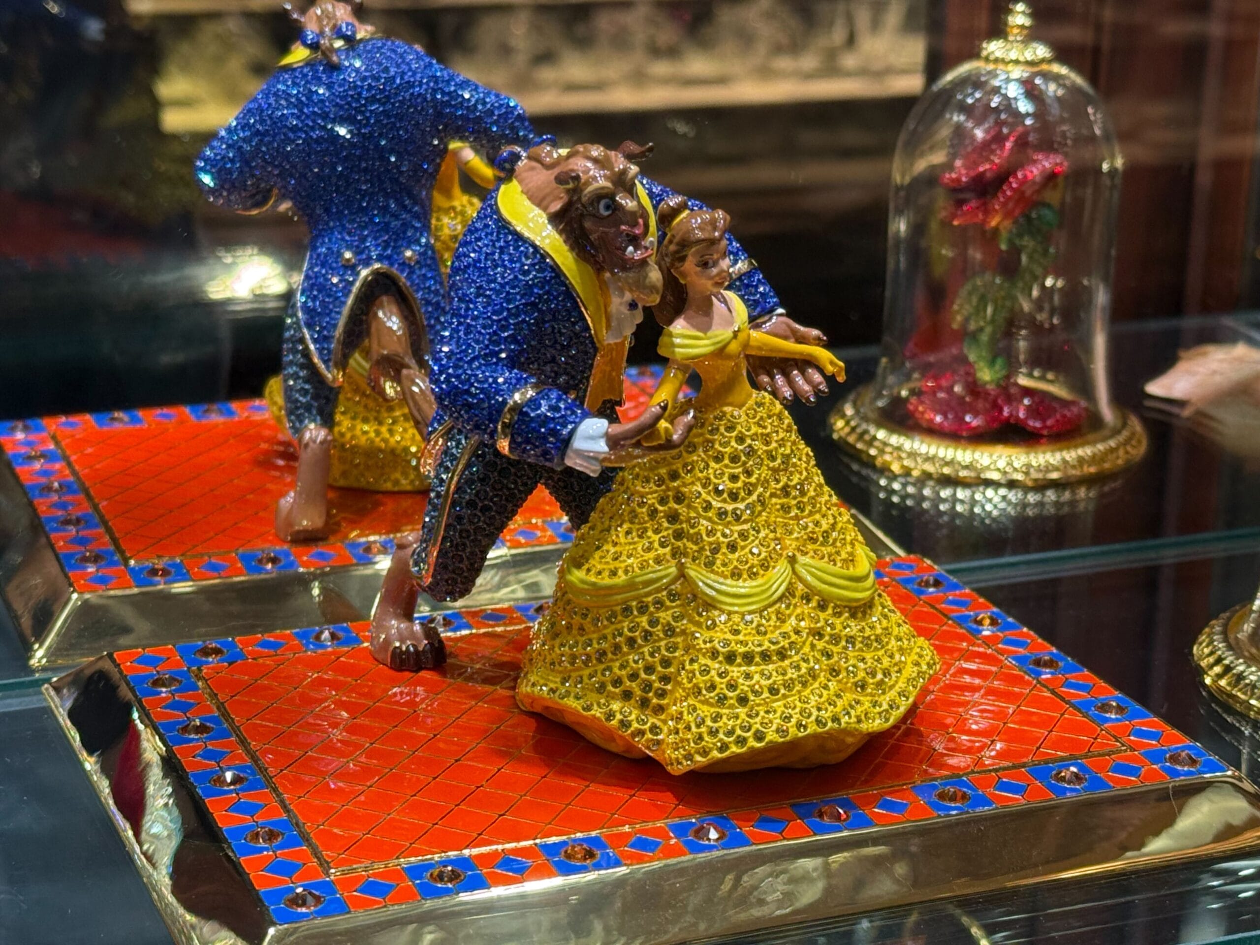 Jeweled Beauty and the Beast figurines dance beside a glass-encased red rose at Crystal Arts in Disneyland.