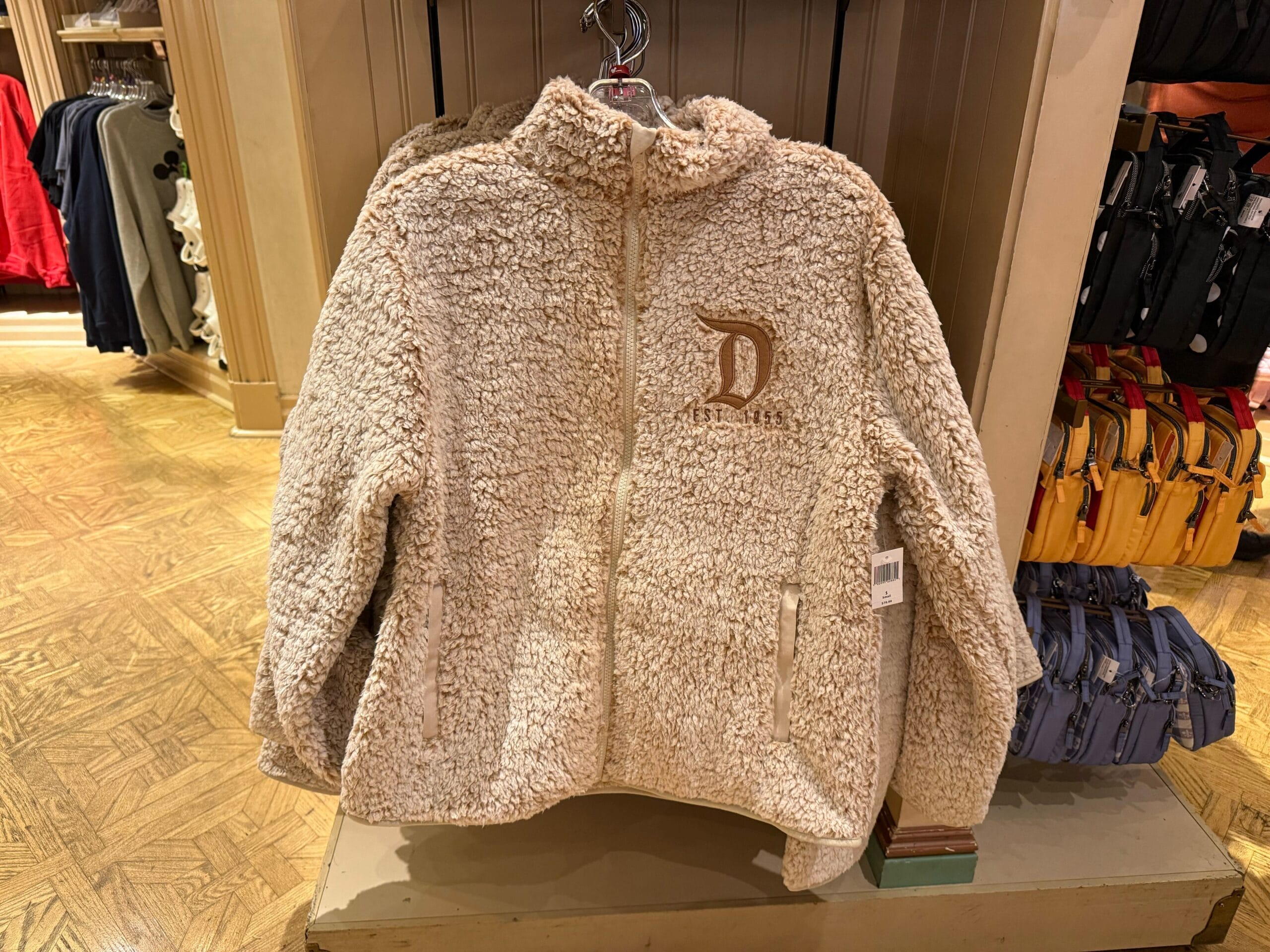 Cream-colored sherpa jacket with "D" logo and front pockets, perfect for layering over your favorite Logo Sweatshirts.