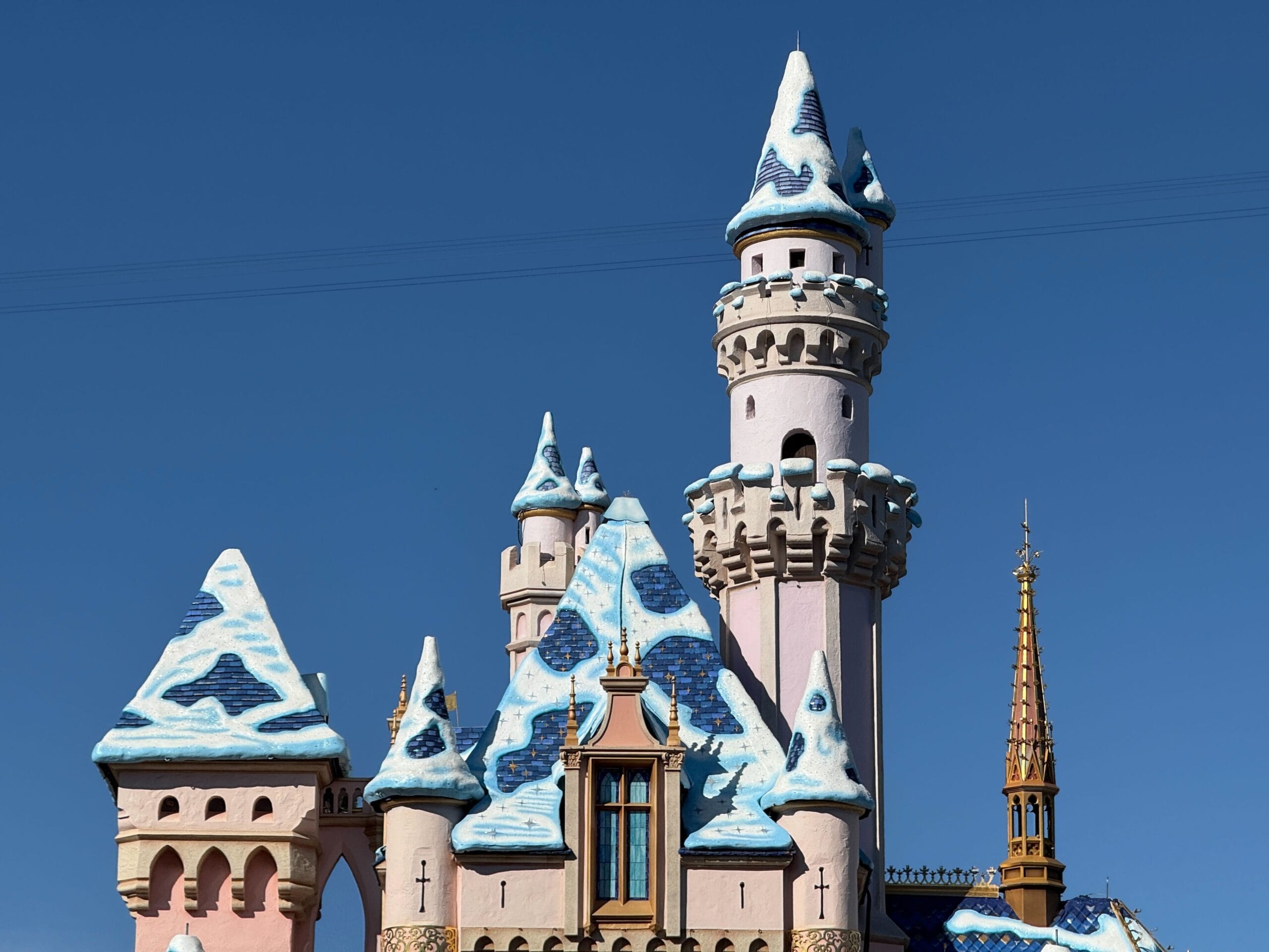 A fairytale castle with blue and white snow-covered rooftops, resembling Disneyland Paris’ castle, against a clear blue sky.