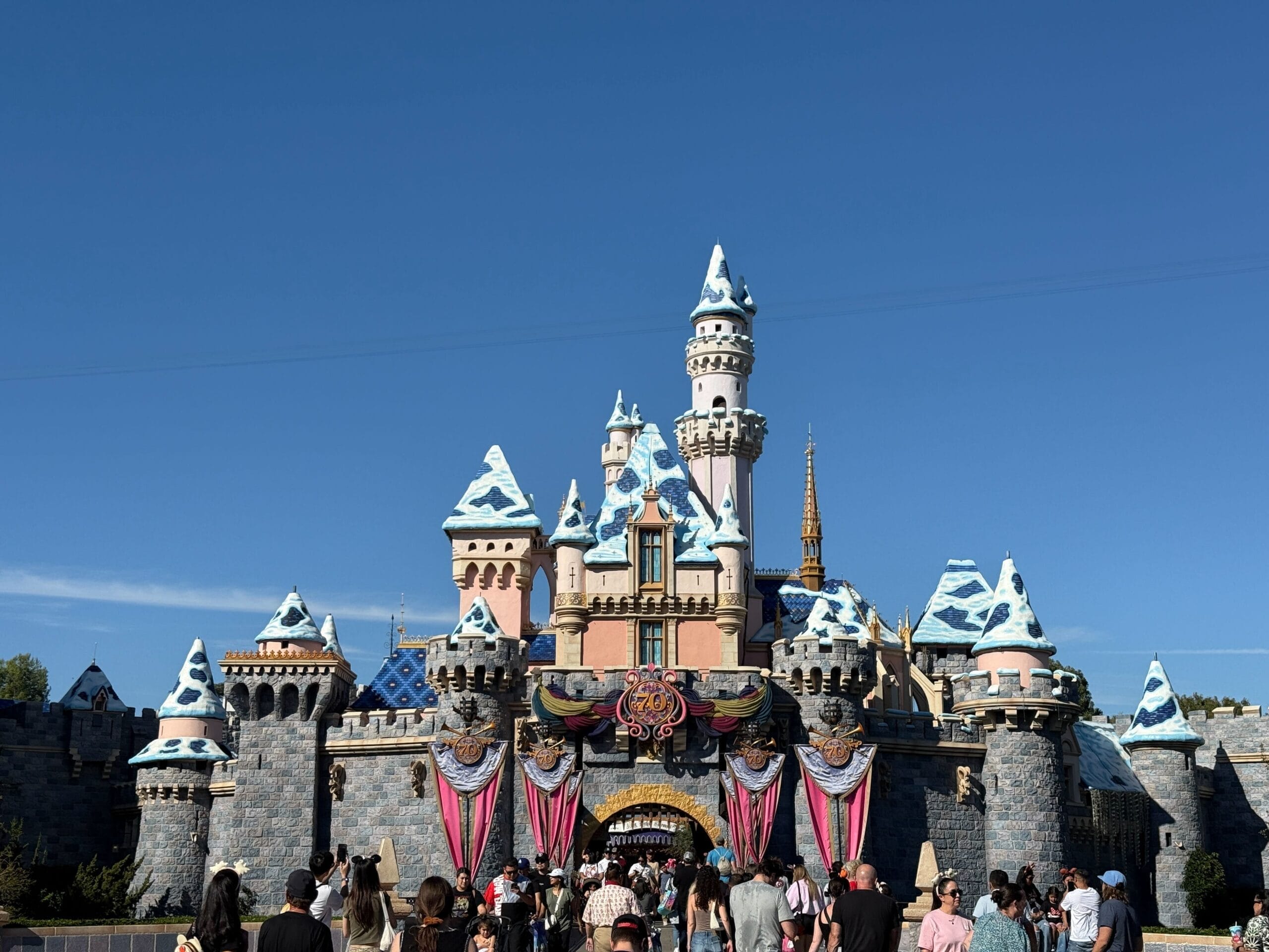 Disneyland’s Sleeping Beauty Castle dusted with snow, bustling crowds, and a crisp blue sky—smaller than Magic Kingdom’s castle.
