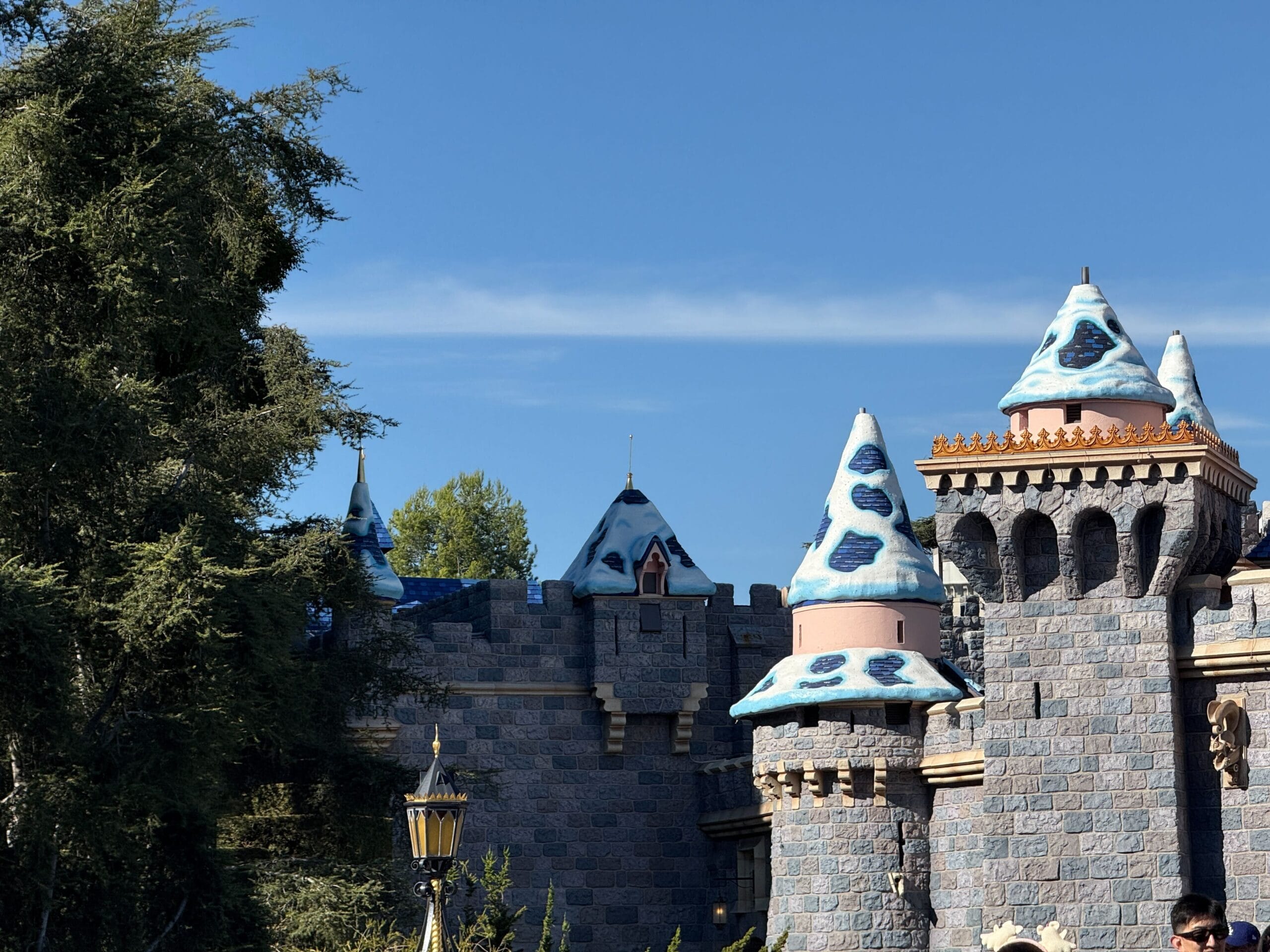A castle with blue and white snow-capped towers, reminiscent of Disneyland's Sleeping Beauty Castle, beneath a clear sky, trees on left.