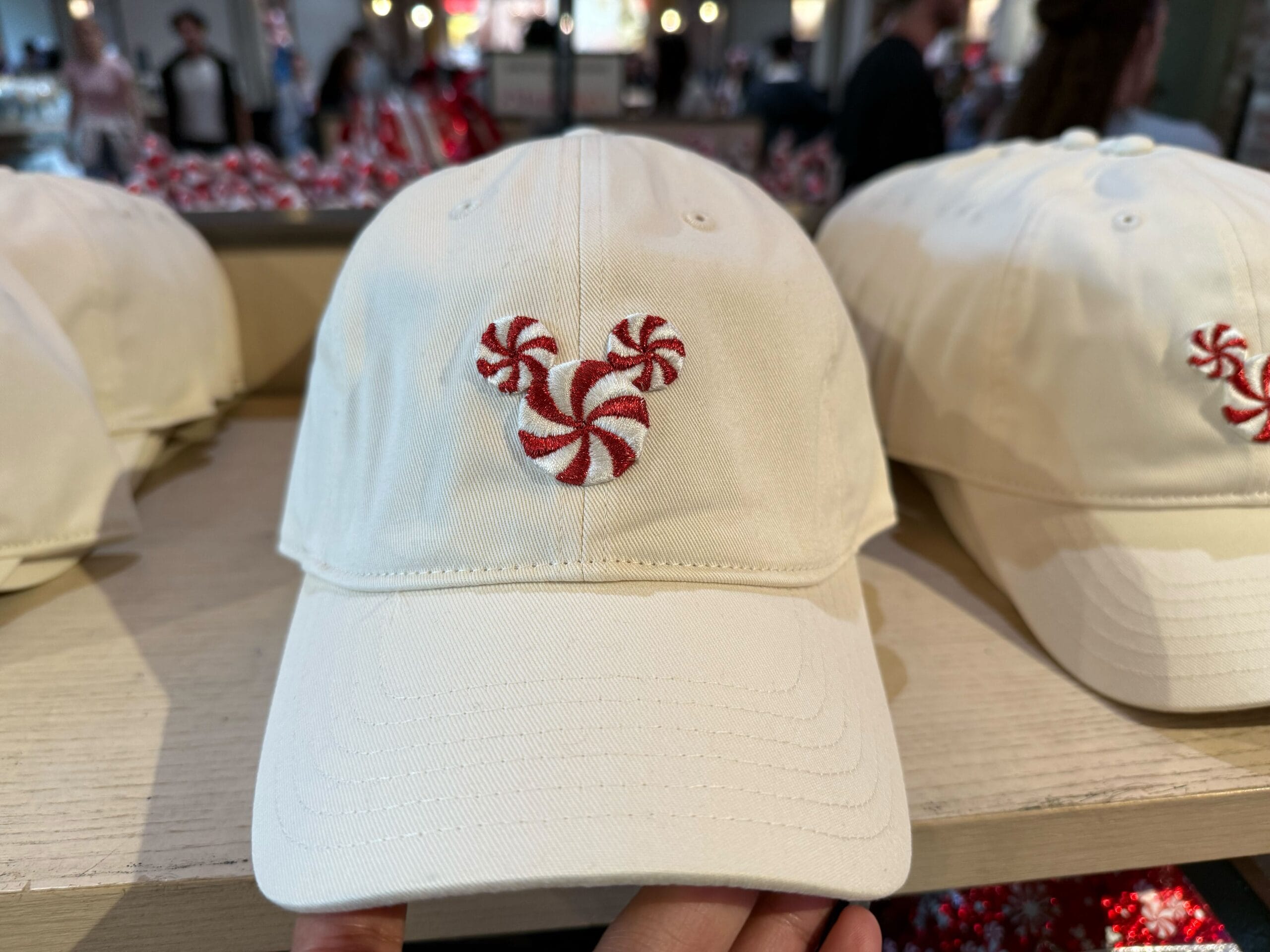 A cream cap featuring a red and white peppermint Mickey Mouse design, a festive touch often seen in Disney Parks merchandise.