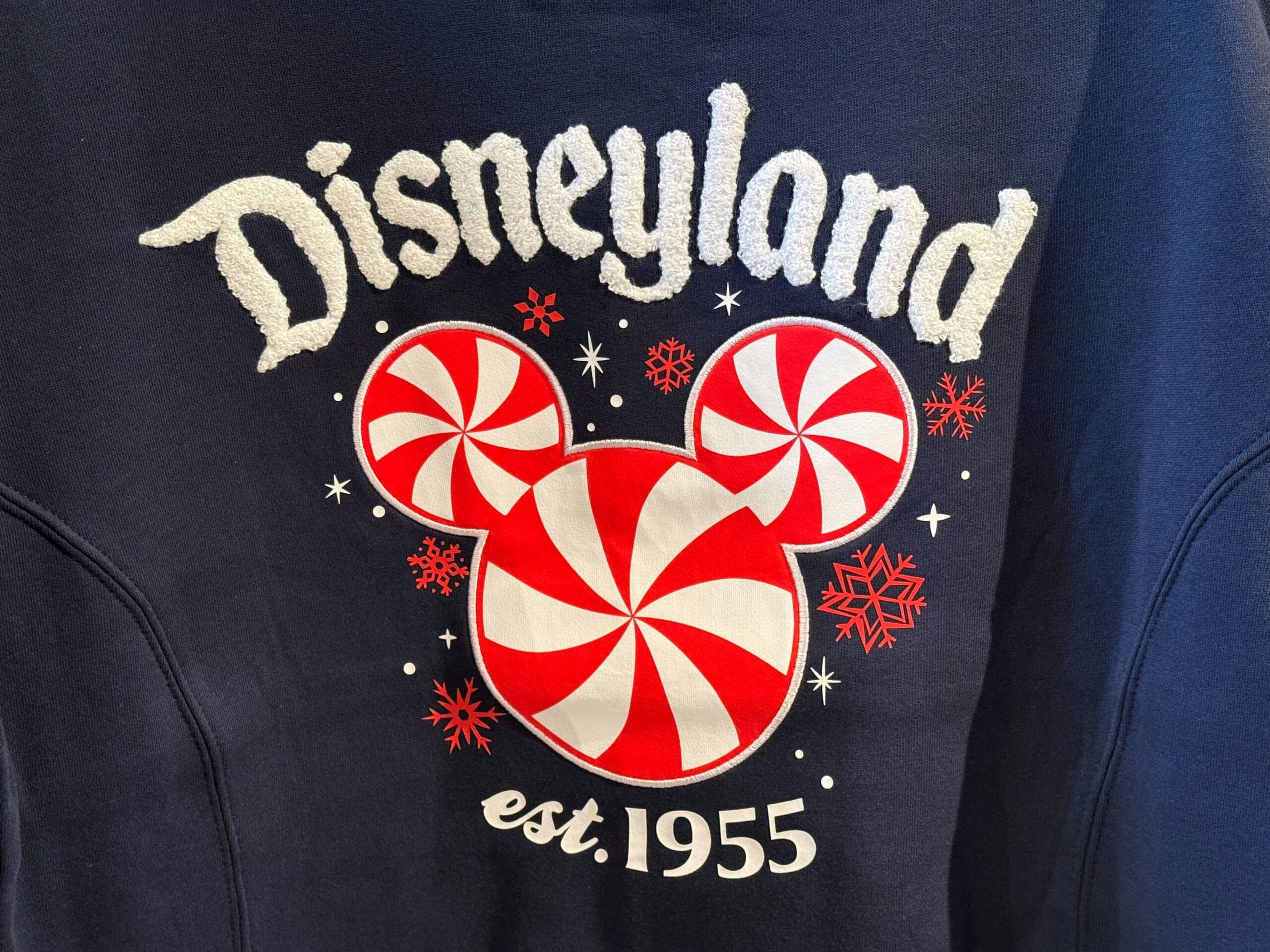 Navy sweatshirt featuring "Disneyland est. 1955" and a Mickey head of peppermint candies, referencing Disneyland CA's history.