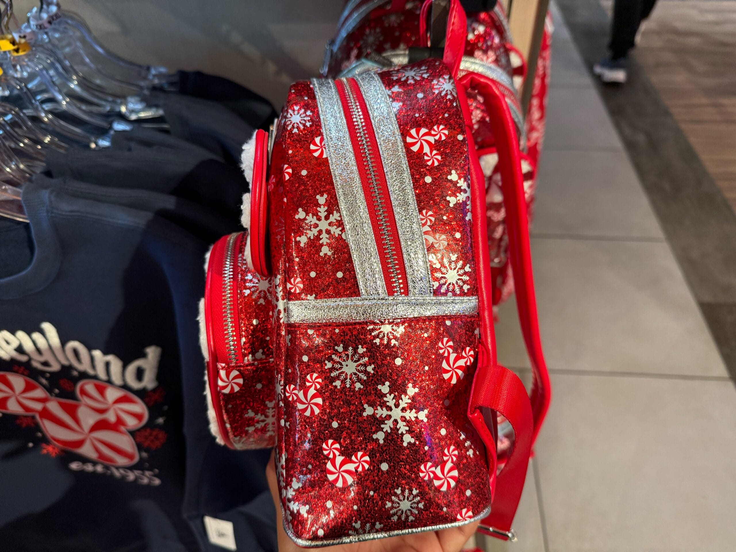 Small red backpack with silver snowflakes and peppermint candy designs, displayed near Disneyland merchandise inside a park shop.