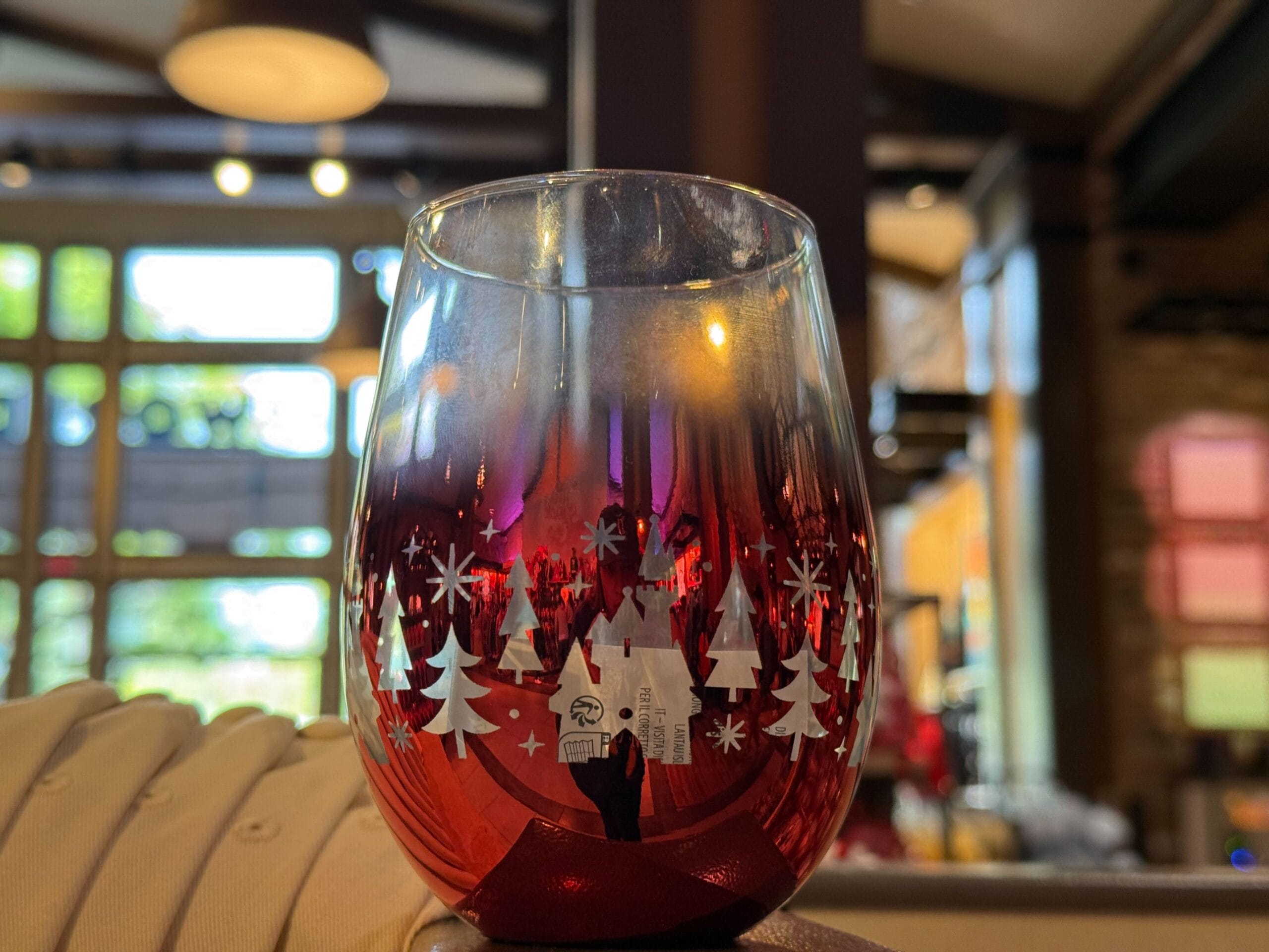 A red Peppermint Collection glass with white tree designs sits on a sunlit table, reminiscent of Disney’s Main Street bakery cafés.