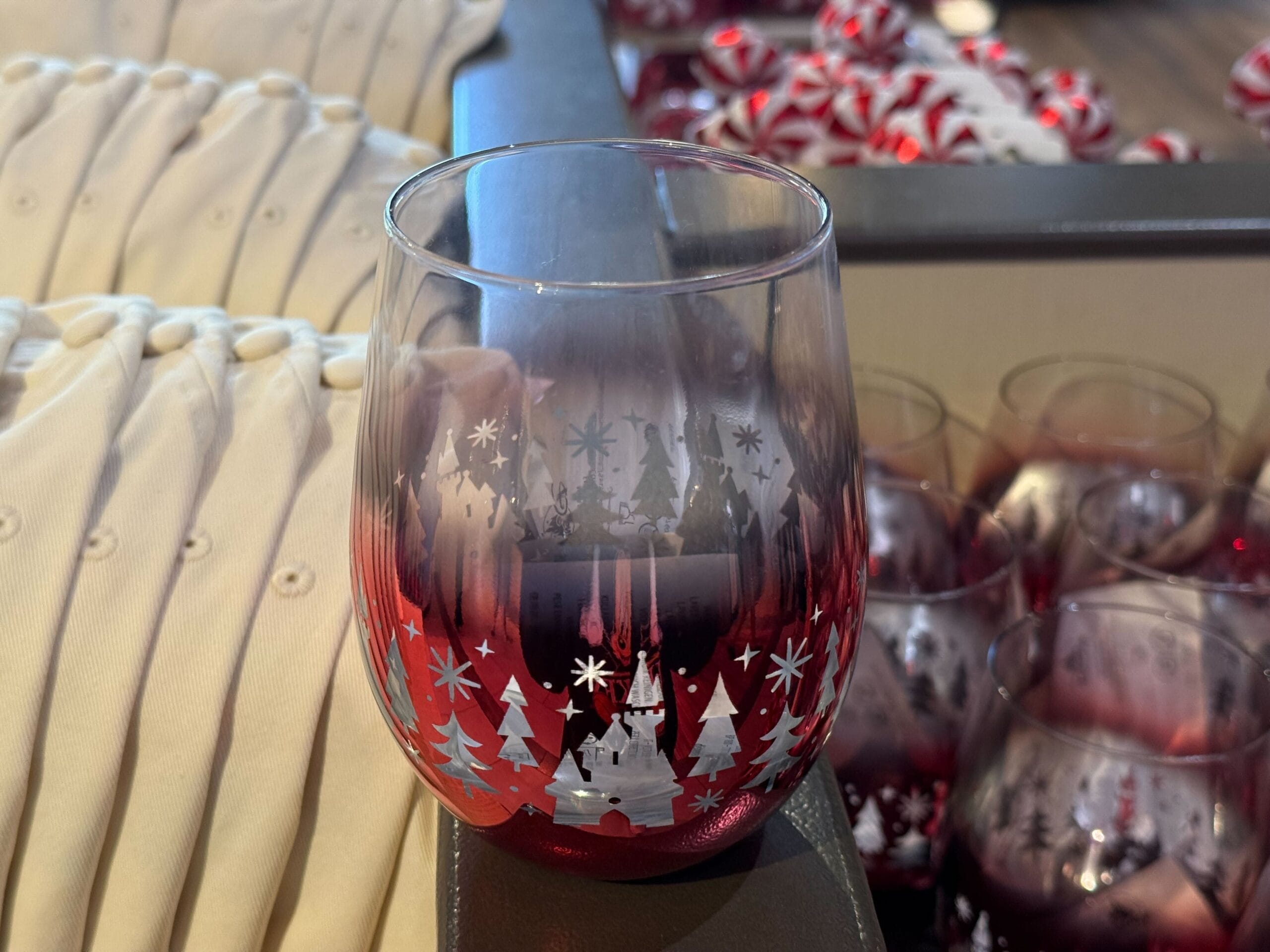 A clear glass of red holiday drink from the Peppermint Collection, with winter trees and snowflakes, sits on a Disney park display.