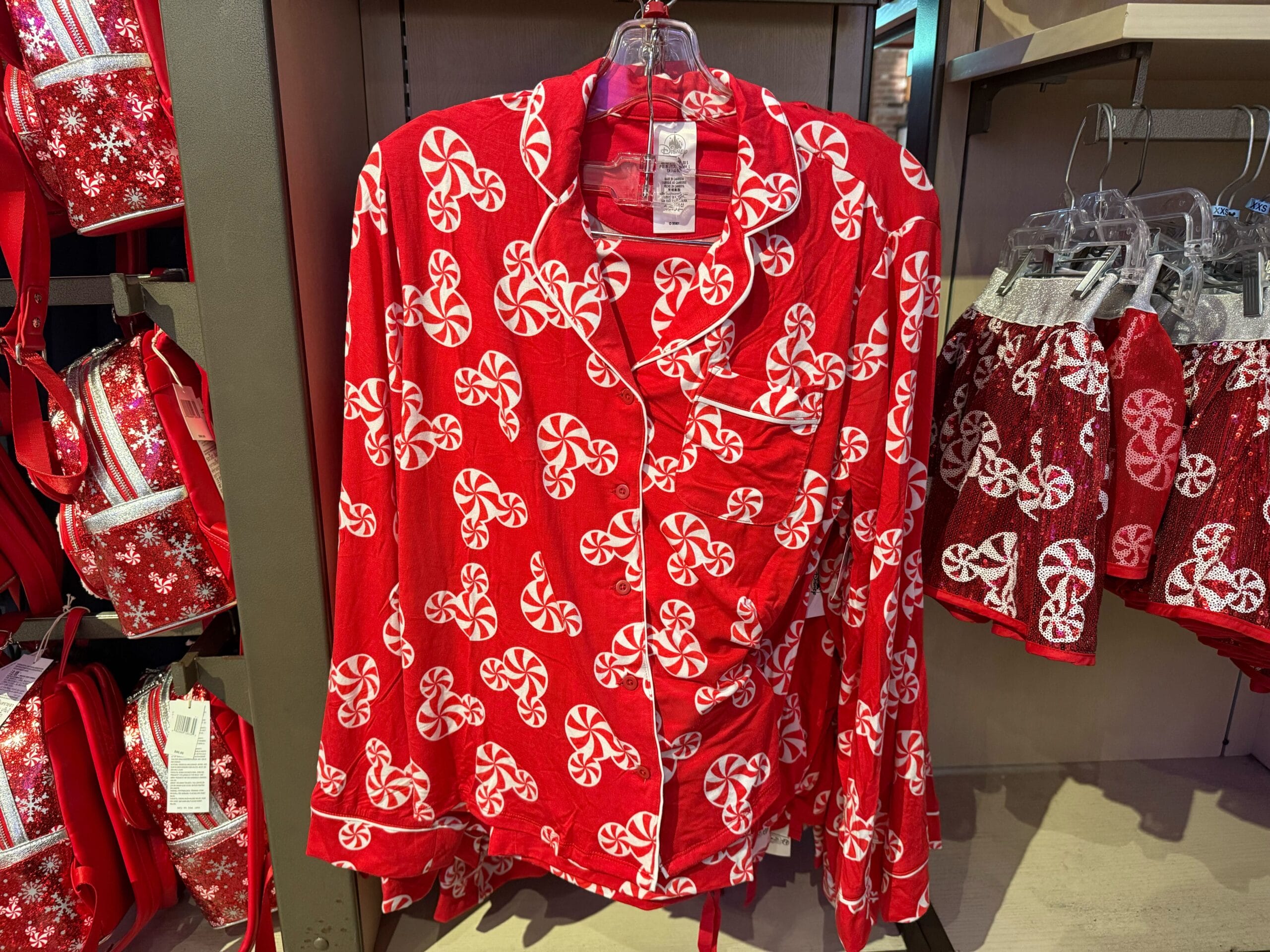Red pajama top with white peppermint candy print, reminiscent of festive Disney merchandise, displayed on a rack in a park store.