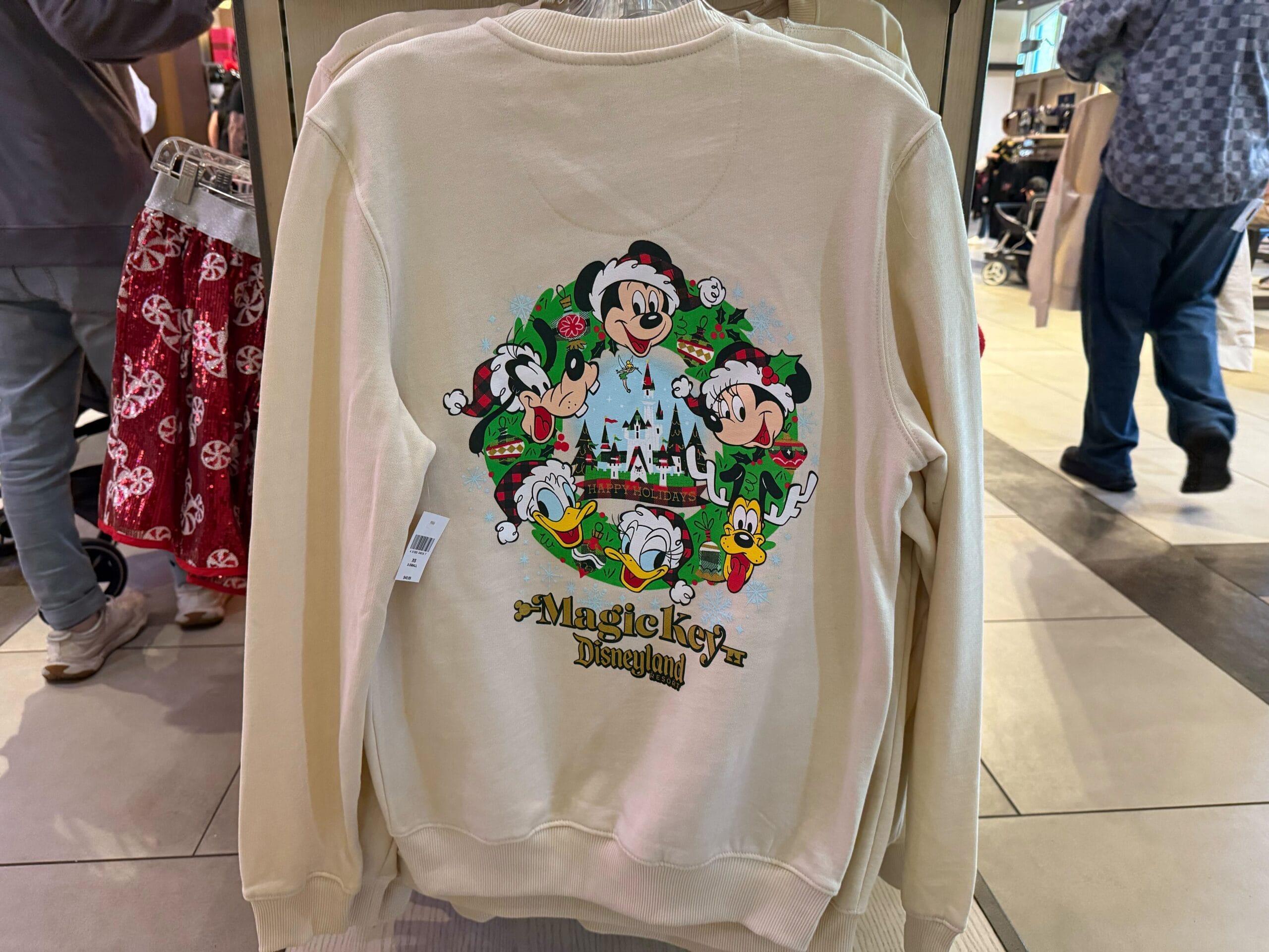Cream Magic Key Sweatshirt featuring Disneyland Christmas art of Mickey and friends around Sleeping Beauty Castle, smaller than Cinderella Castle.