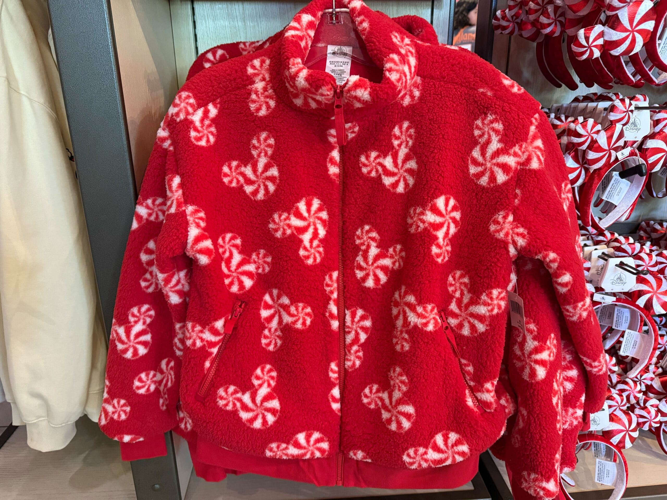 Red fleece jacket covered in white Mickey Mouse peppermint candy shapes on a display rack at a Disney park merchandise shop.