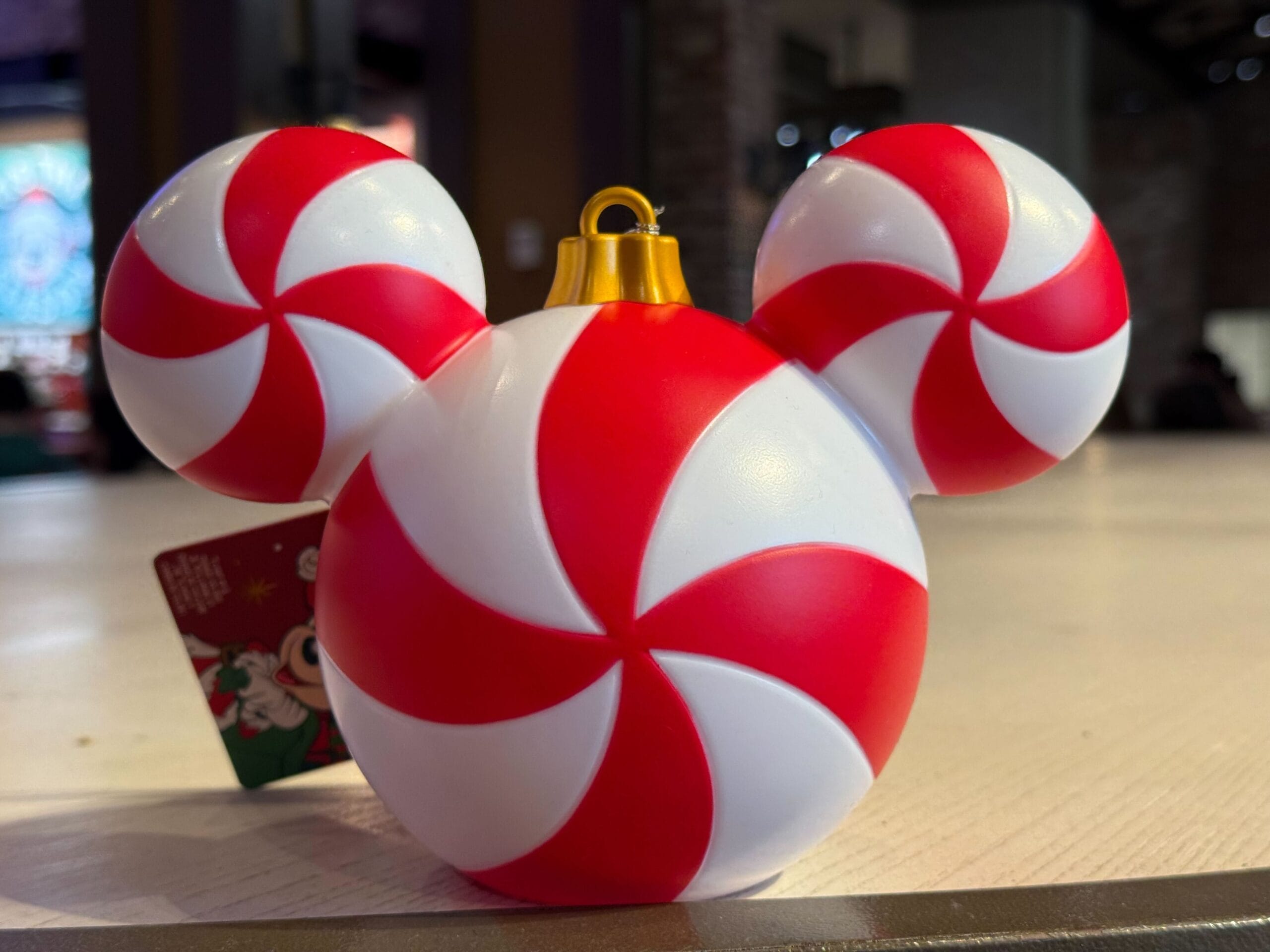 A Disney Parks Christmas ornament shaped like Mickey Mouse, featuring red and white peppermint swirls, perfect for festive decor.