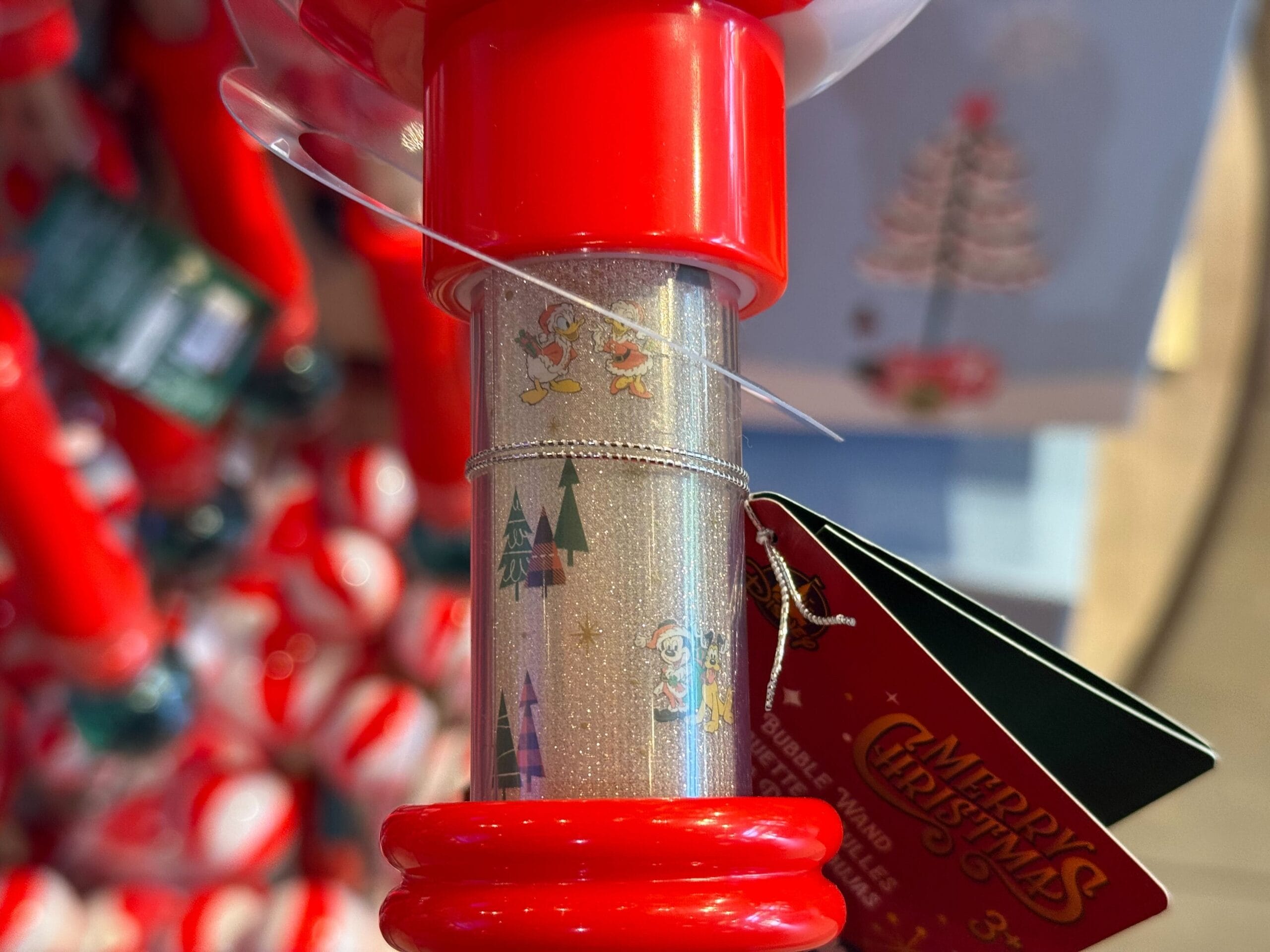 Close-up of a Christmas-themed wand with festive trees and Disney characters, featuring a "Merry Christmas" tag, likely from the parks.