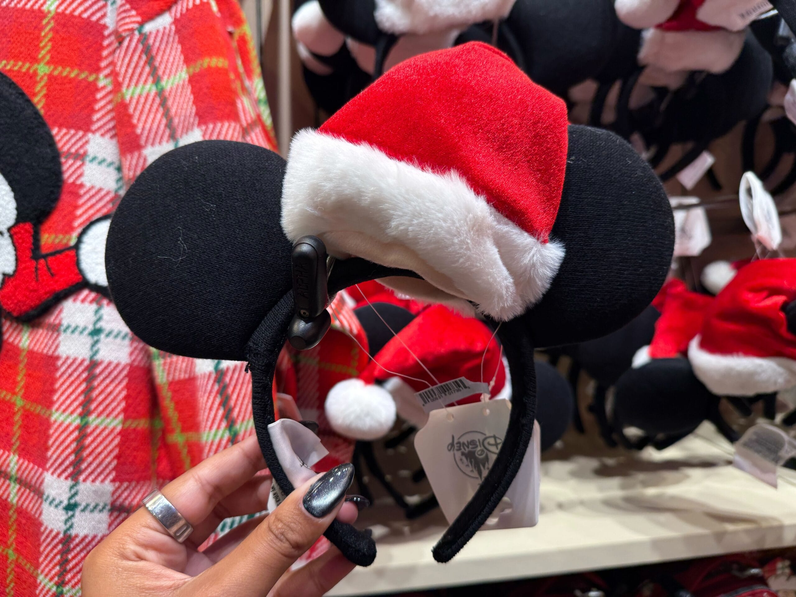 A hand holds a Mickey Mouse ear headband with a Santa hat, festive Disneyland Christmas merchandise in the park's gift shop.