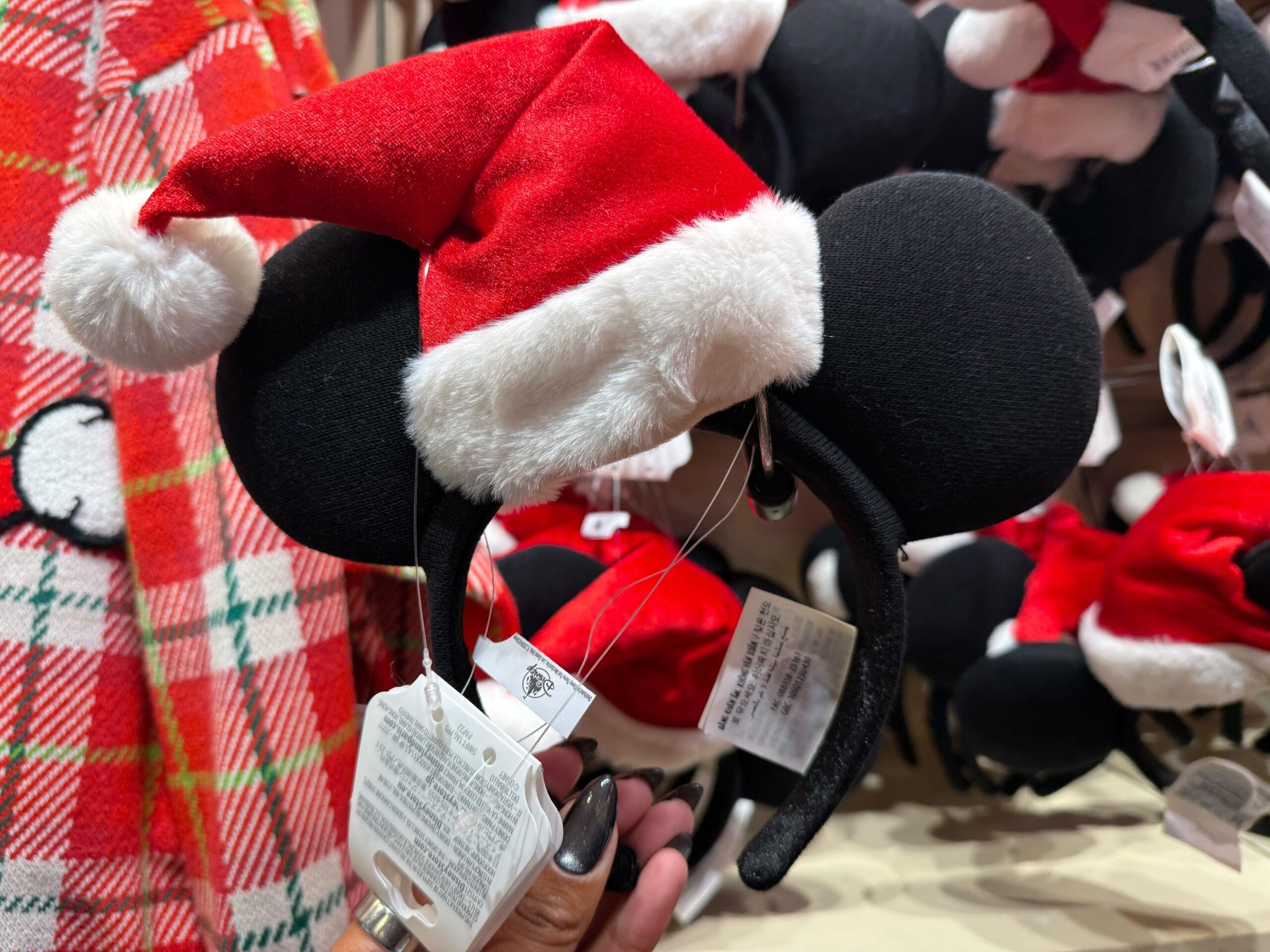A hand holds Mickey Mouse ears topped with a red Santa hat, featured in a Disneyland holiday display—perfect park souvenir.