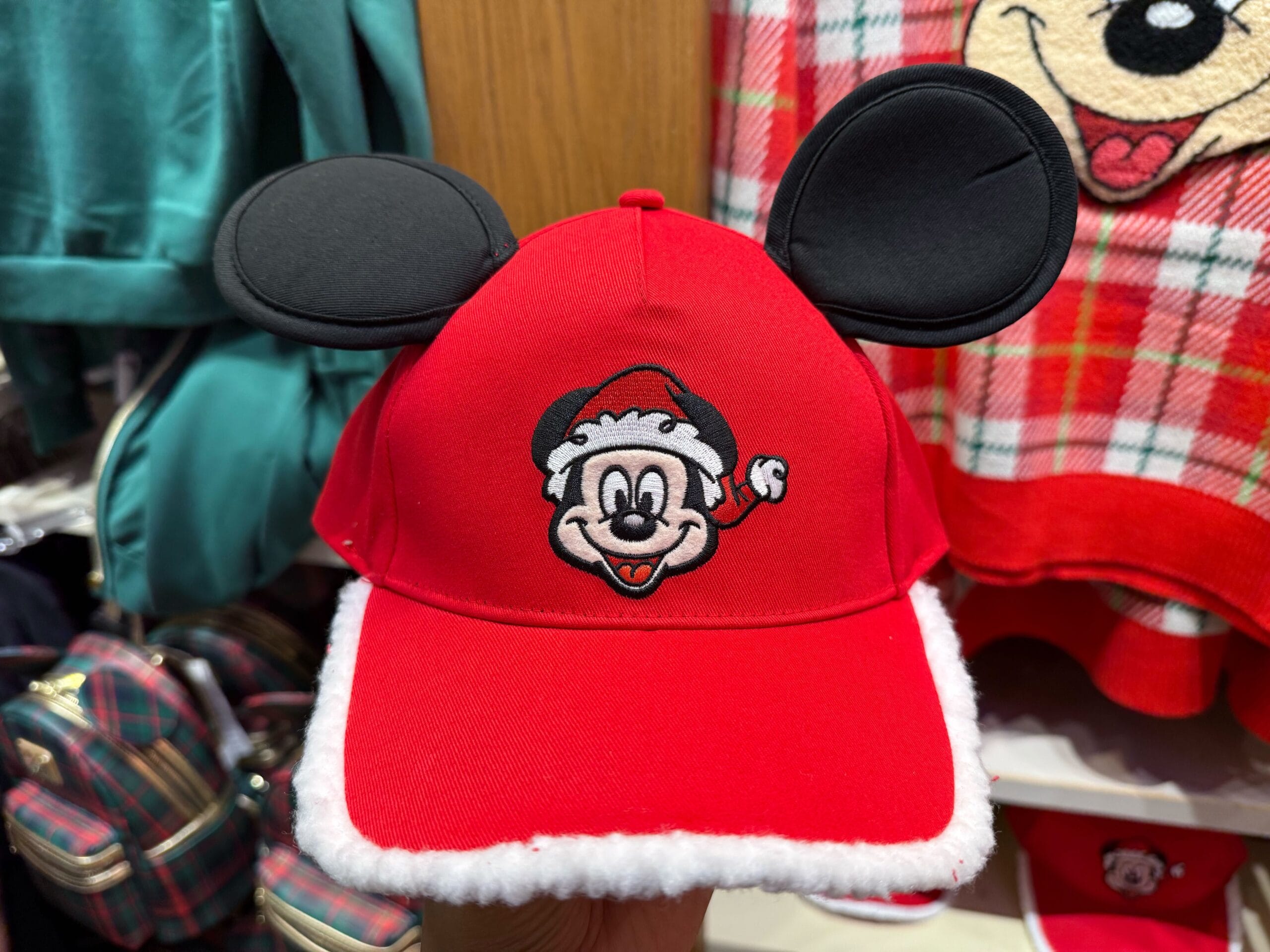 Disneyland Christmas merchandise: red Santa hat with Mickey Mouse ears, displayed among festive plaid items in a park shop.