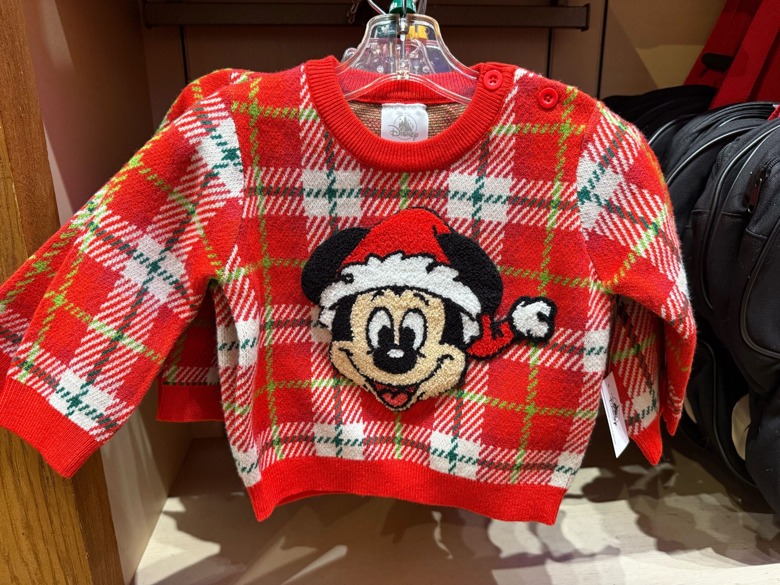 Red plaid sweater with Santa hat Mickey Mouse, part of Disneyland’s holiday merch, seen in a Disney park store display.