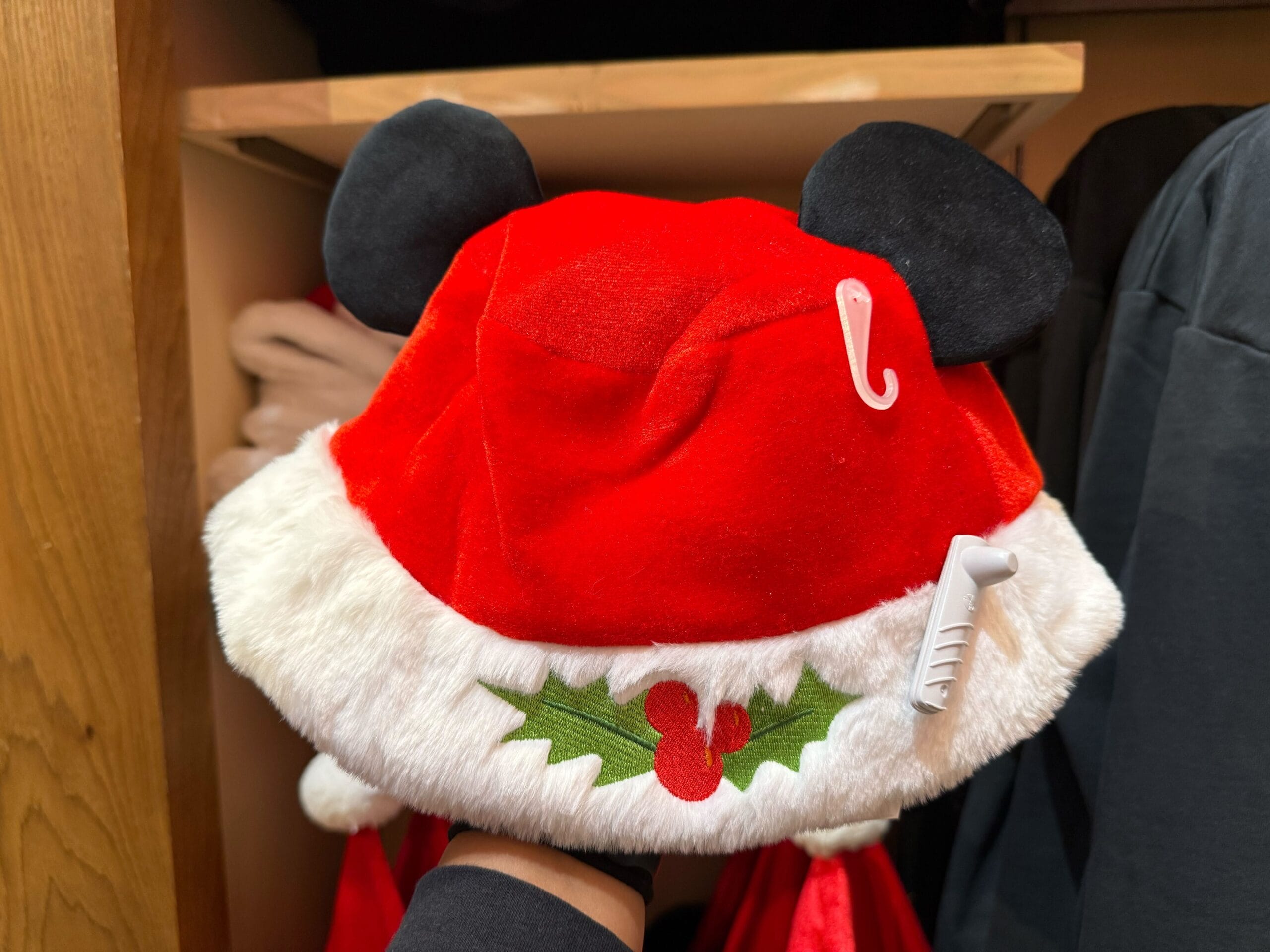 A festive red Santa hat featuring Mickey Mouse ears, part of Disneyland holiday merchandise, displayed in a park shop.