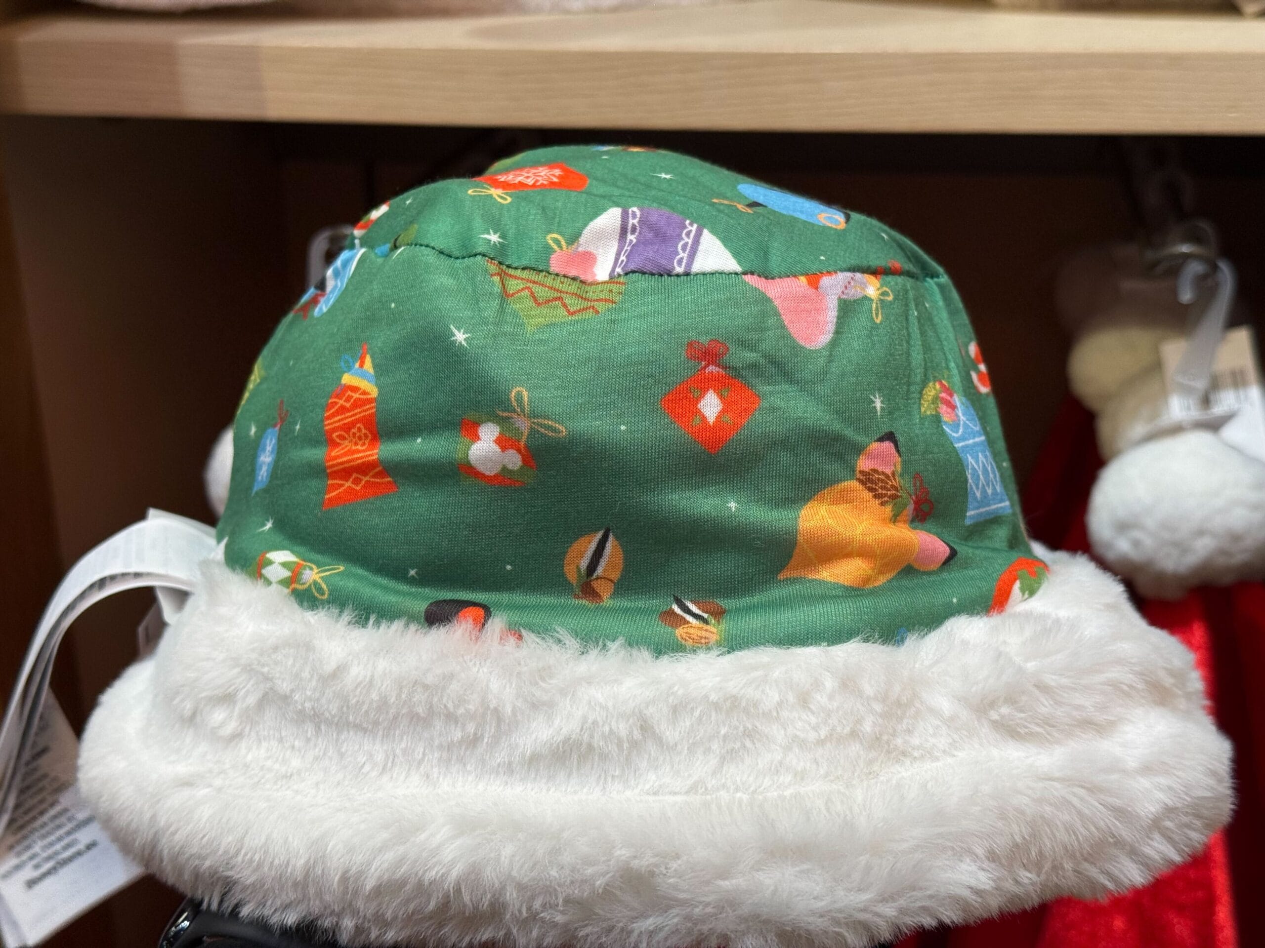 Green holiday hat with white faux fur trim from the Peppermint Collection, displayed on a festive shelf at a Disney park store.