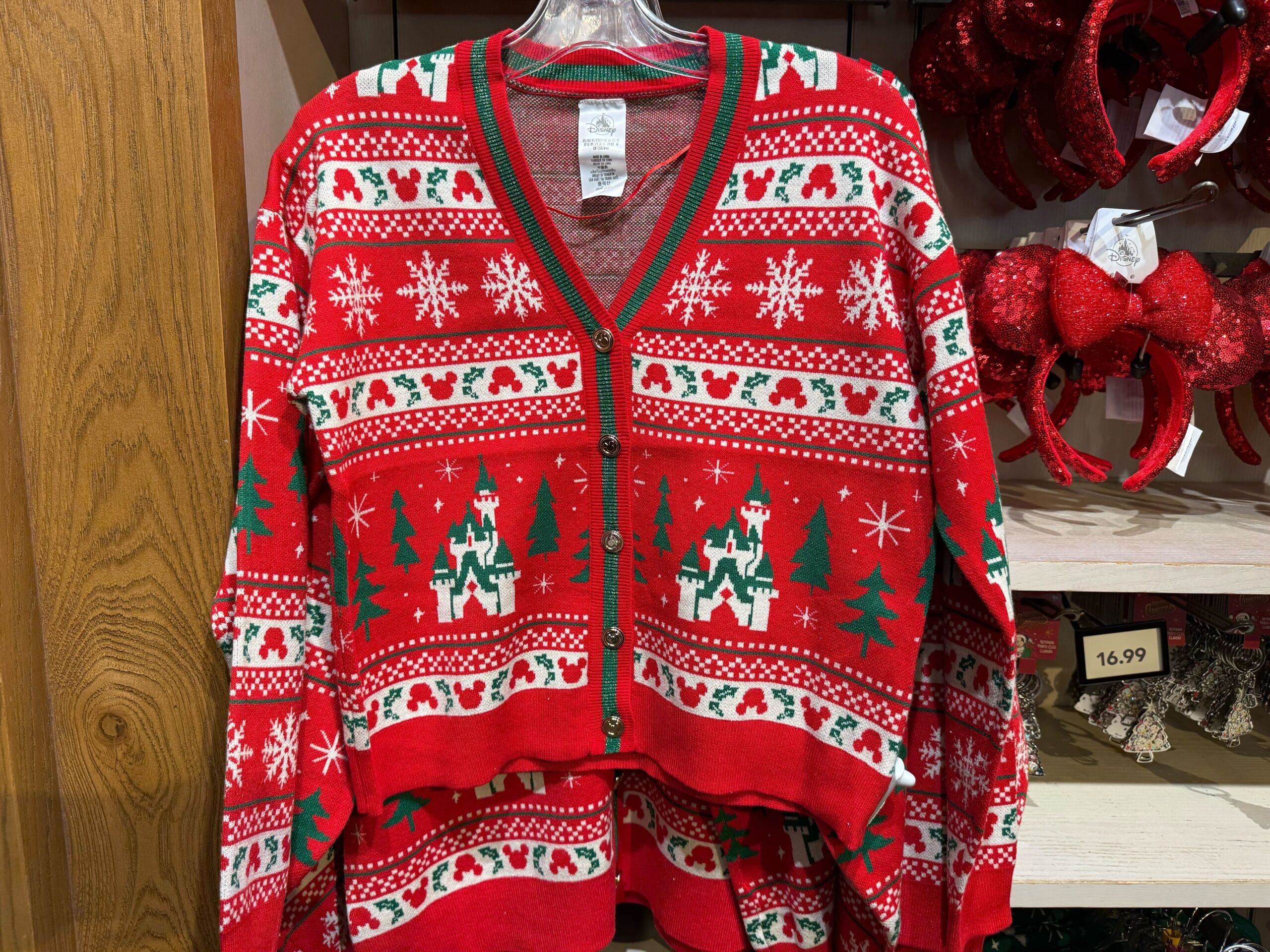 Red Christmas sweater with green trim, featuring castle patterns reminiscent of Disneyland’s Sleeping Beauty Castle, from park merch.