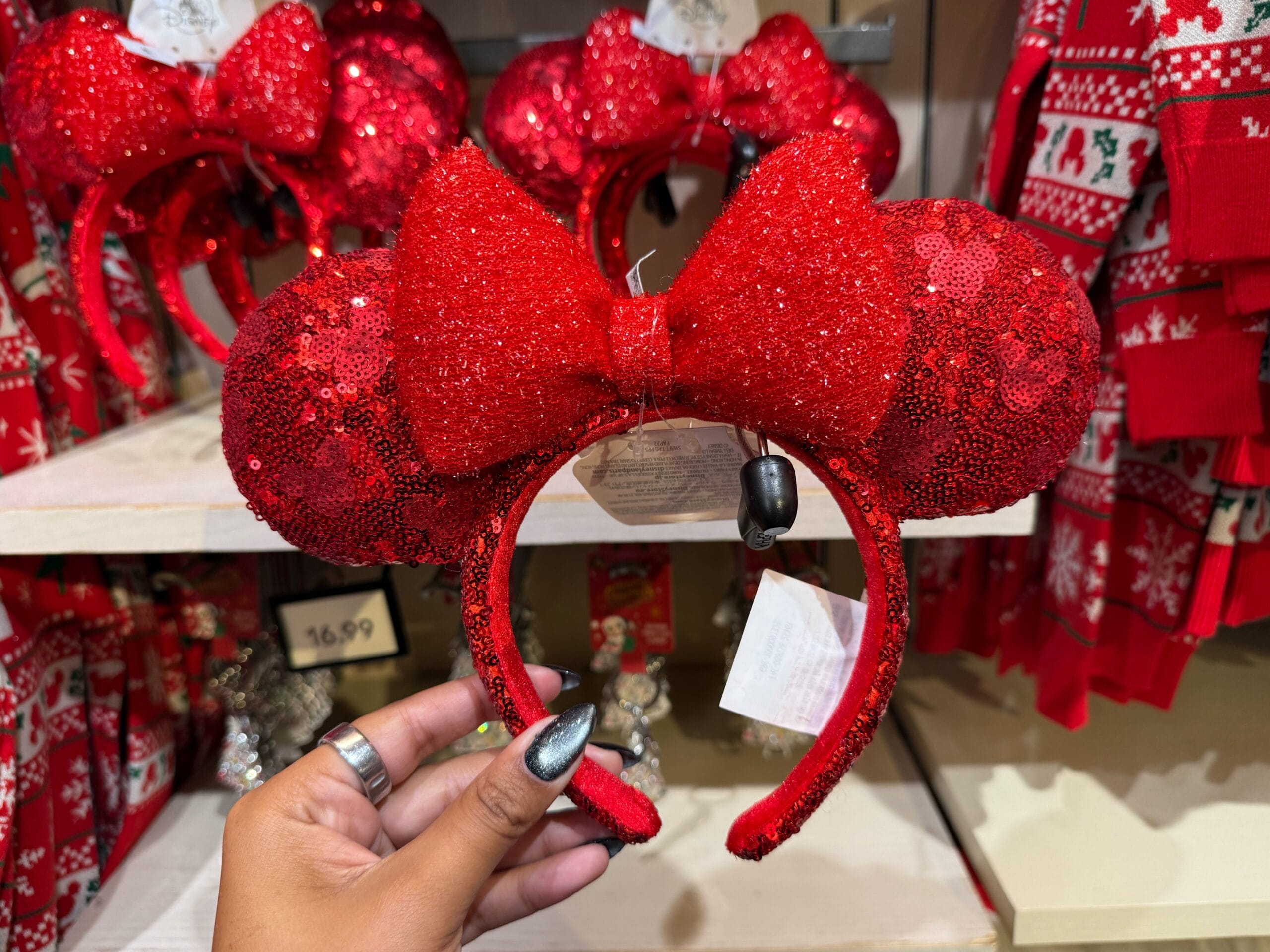 A hand displays a glittery red Minnie Mouse ear headband from the Peppermint Collection inside a Disney park shop.