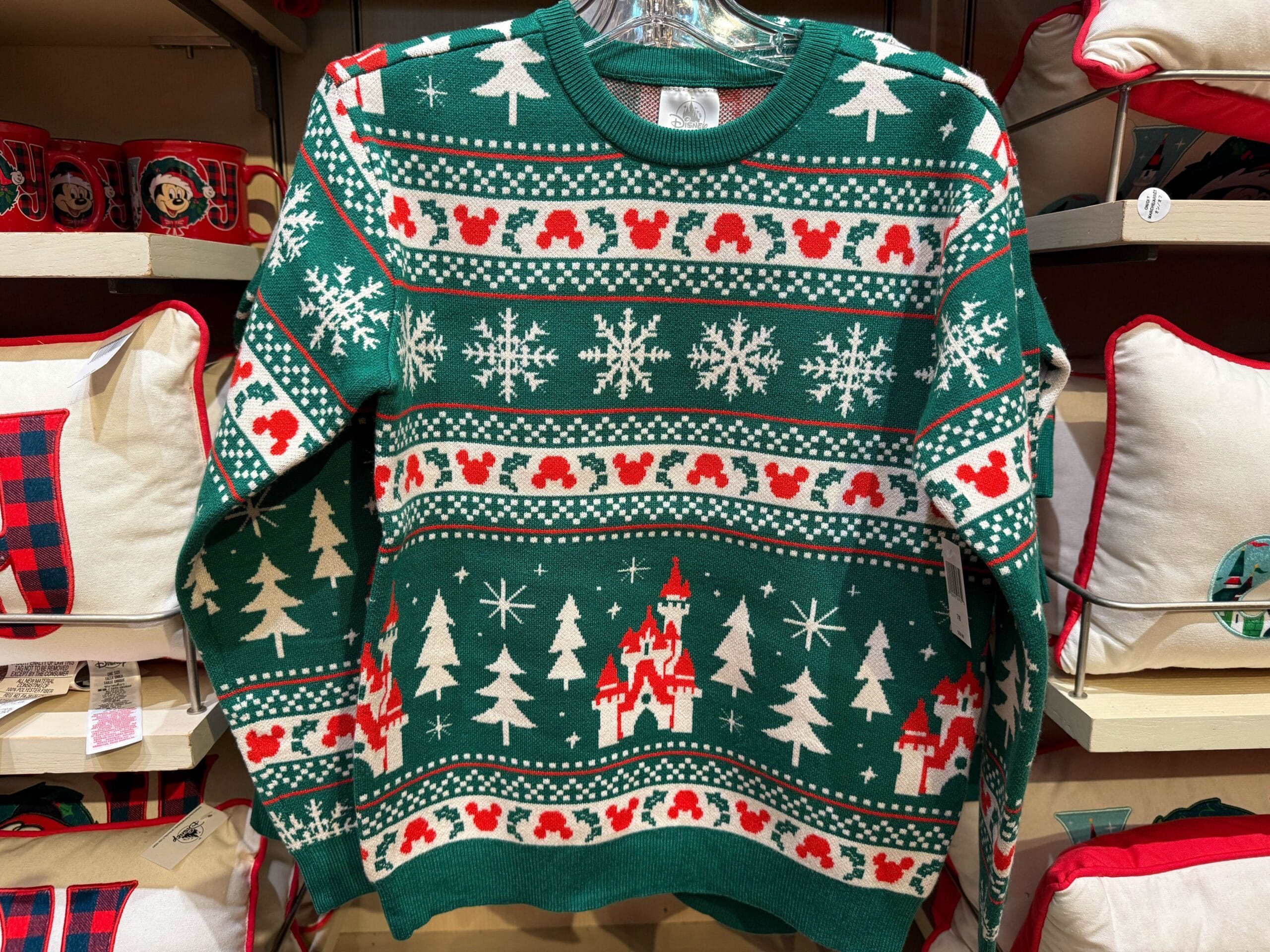 Green holiday sweater with white snowflakes, trees, red mouse heads, and stylized castles resembling Disneyland’s Sleeping Beauty Castle.