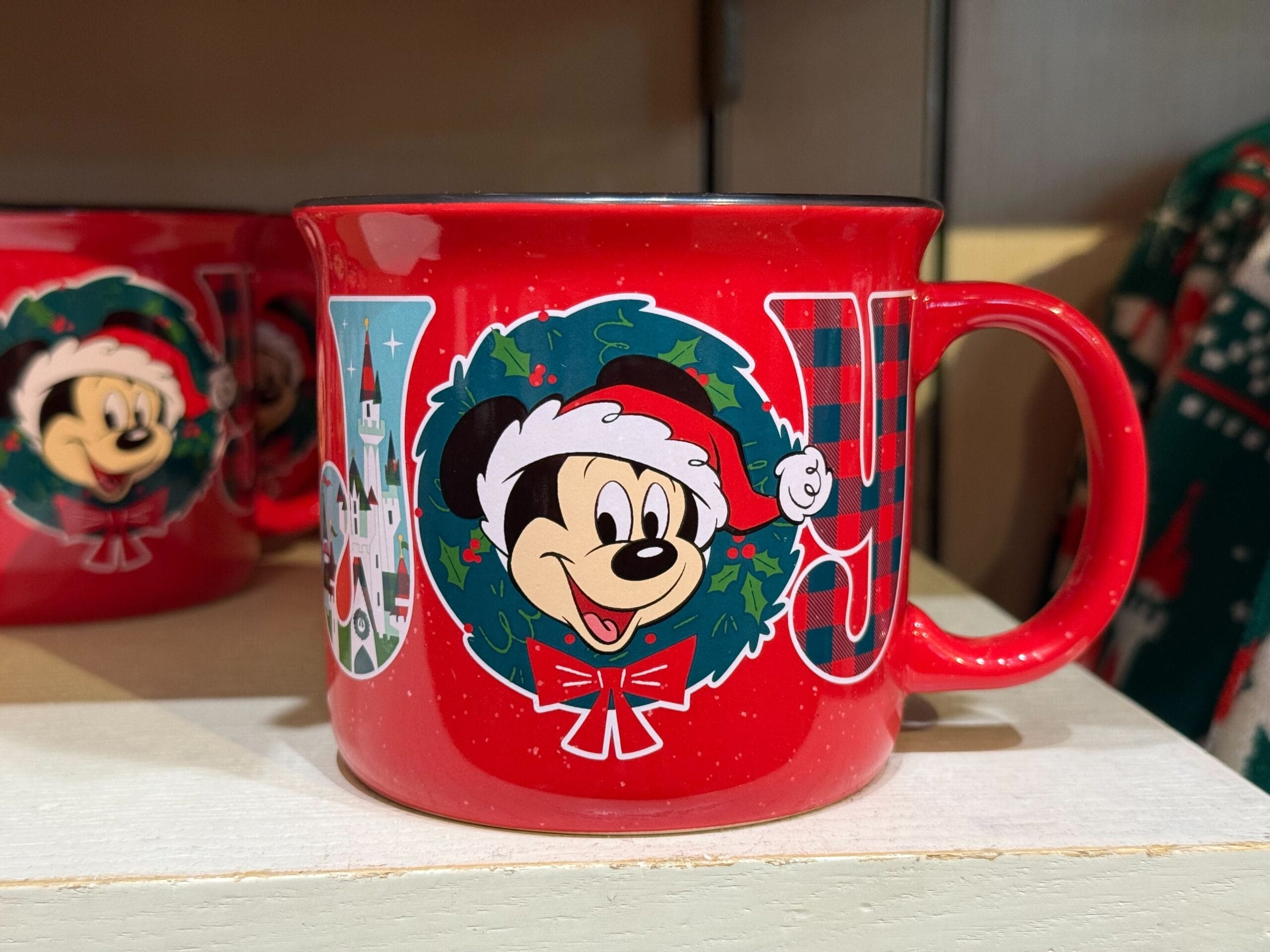 Red mug with “JOY,” Mickey Mouse in holiday attire, and wreath; Disneyland Christmas merch—no castle, but classic park style.