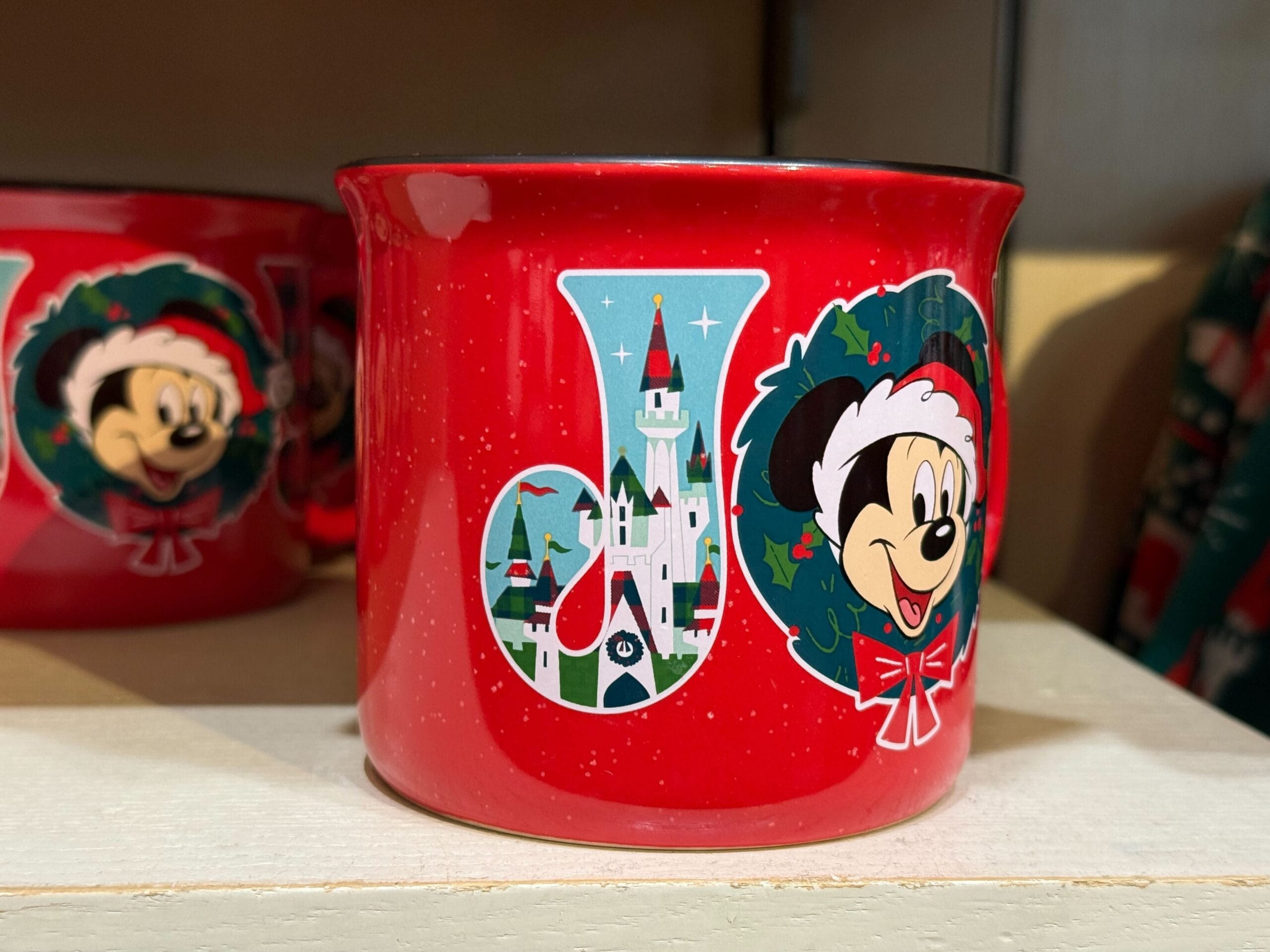 Red mug with “JOY,” Minnie in a wreath, and a castle resembling the classic Disneyland design—Disney Parks holiday merchandise display.