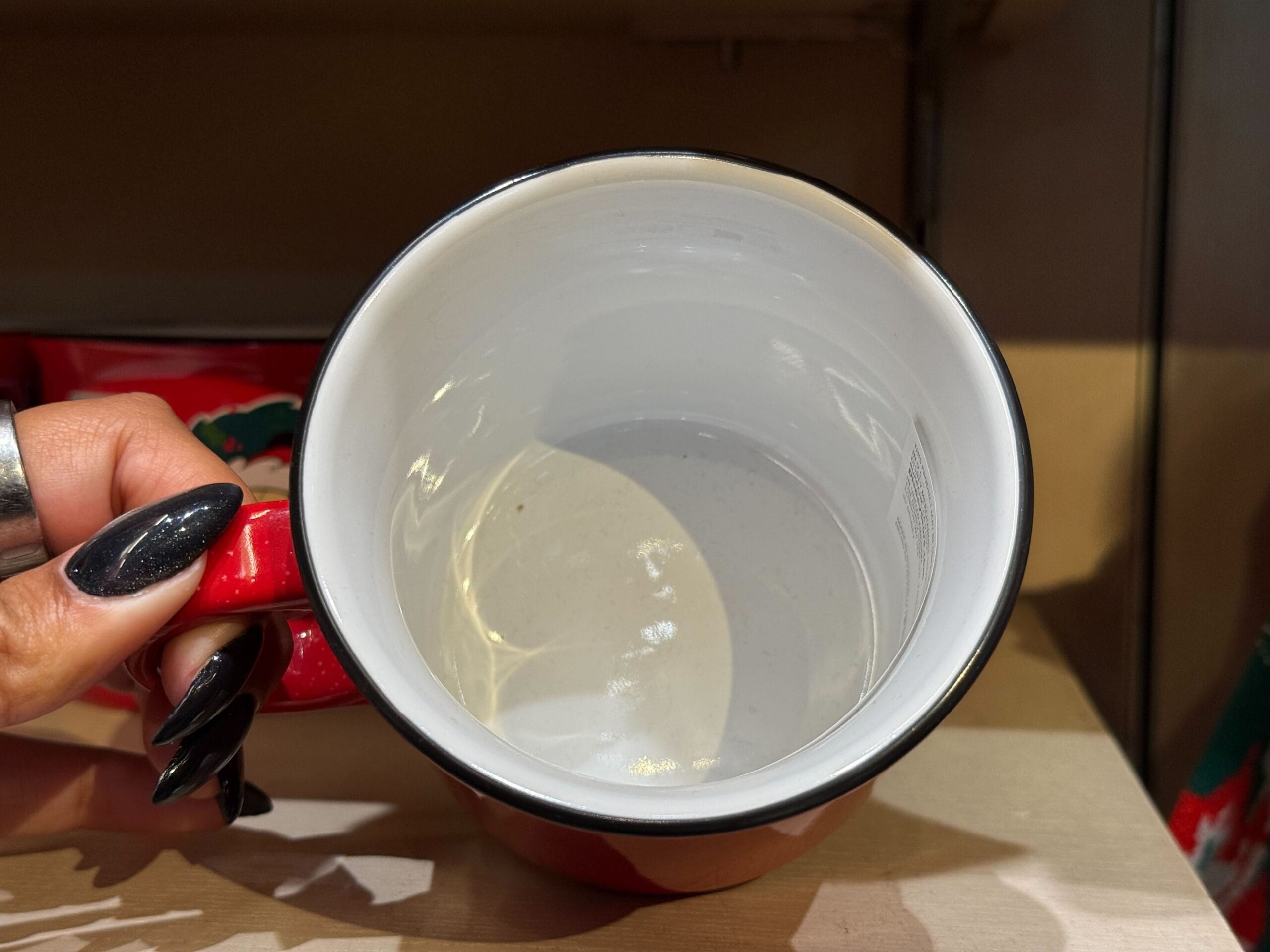A hand with long black nails holds a red Peppermint Collection mug, its white interior as pristine as Cinderella Castle’s walls.
