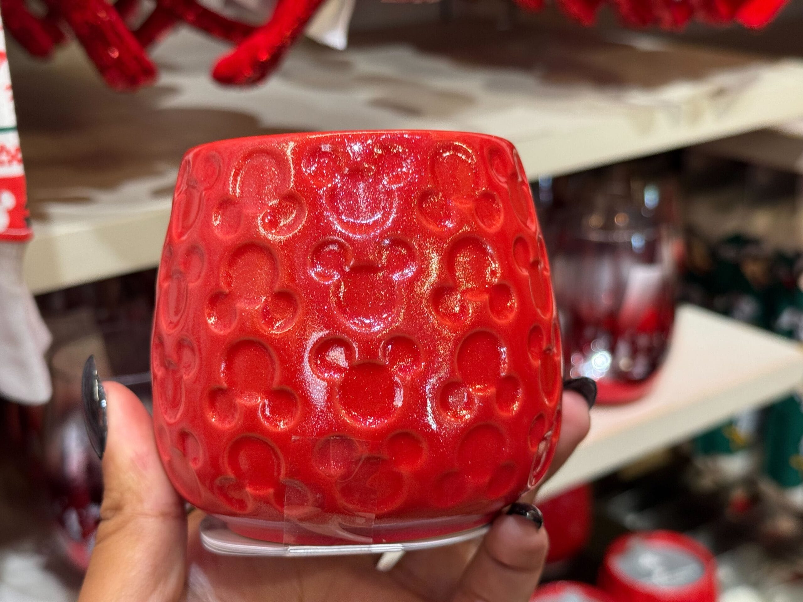 A hand holds a shiny red cup with embossed Mickey Mouse heads from Disneyland’s Christmas display, near Sleeping Beauty Castle.