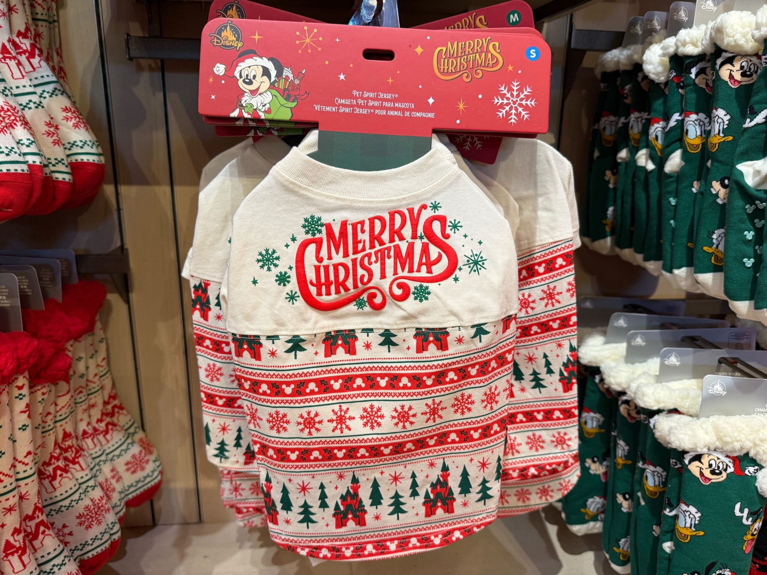 Dog shirt from the Peppermint Collection with “Merry Christmas” in red and green, displayed in a shop at a Disney park.